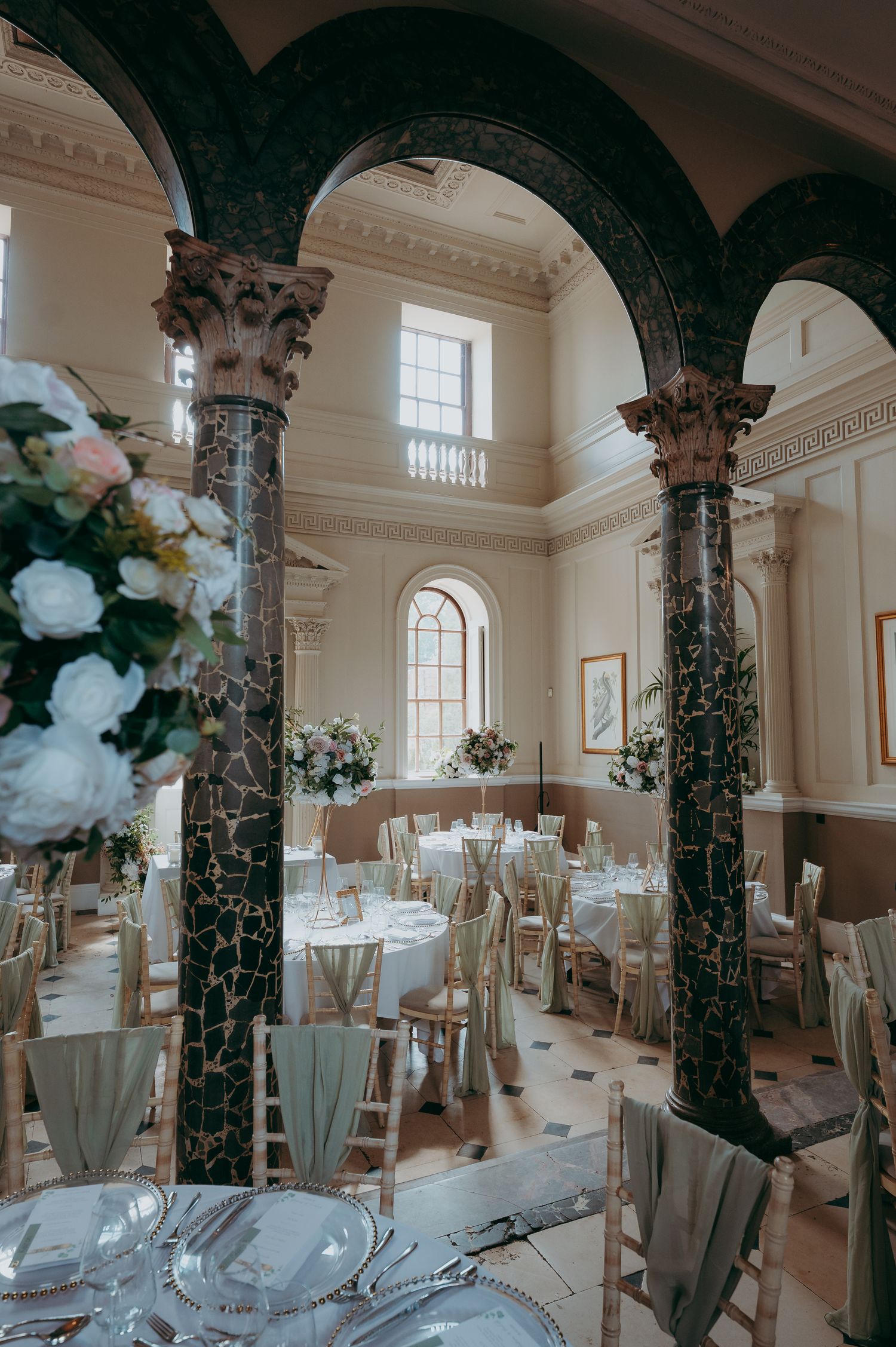 Elegant wedding reception hall with marble columns, arched ceilings, round tables, and floral centerpieces in a grand venue.
