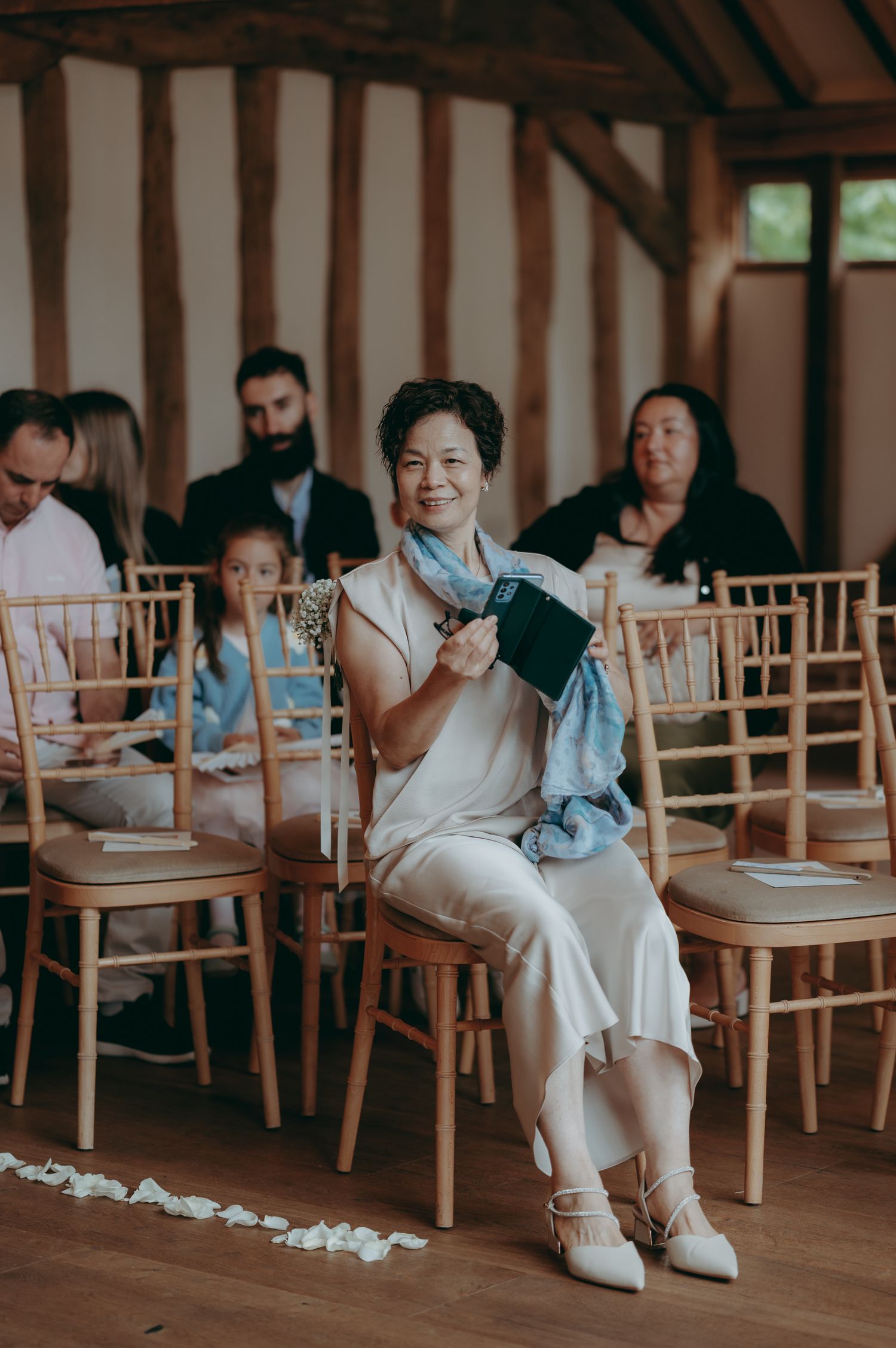 Elegant woman in white dress holding a book at a wedding ceremony in a rustic barn venue.
