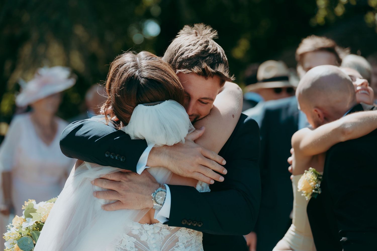Bride and groom sharing a heartfelt hug at outdoor wedding ceremony surrounded by guests.