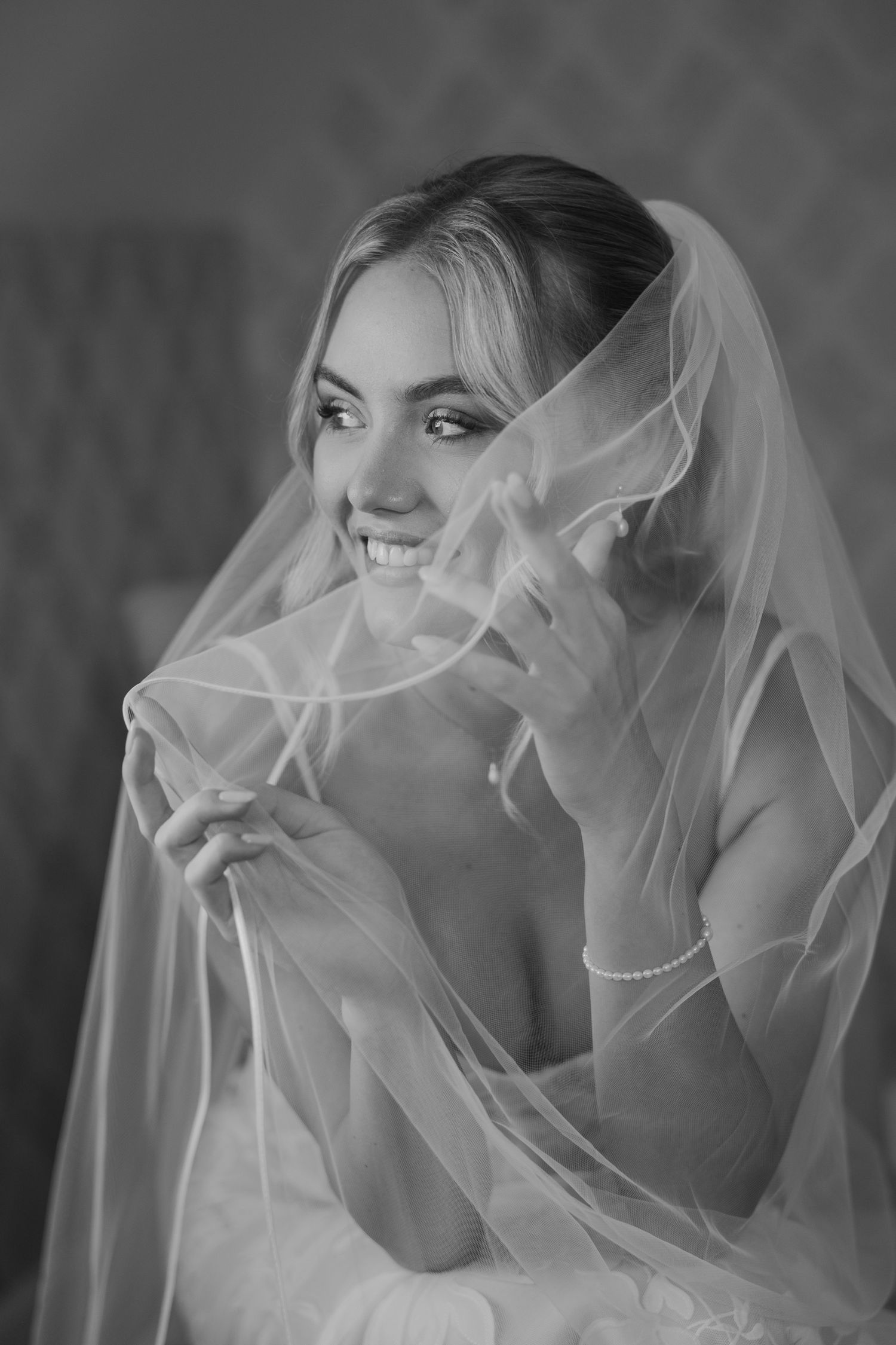 Smiling bride in white veil and gown poses elegantly in black and white wedding portrait photo.