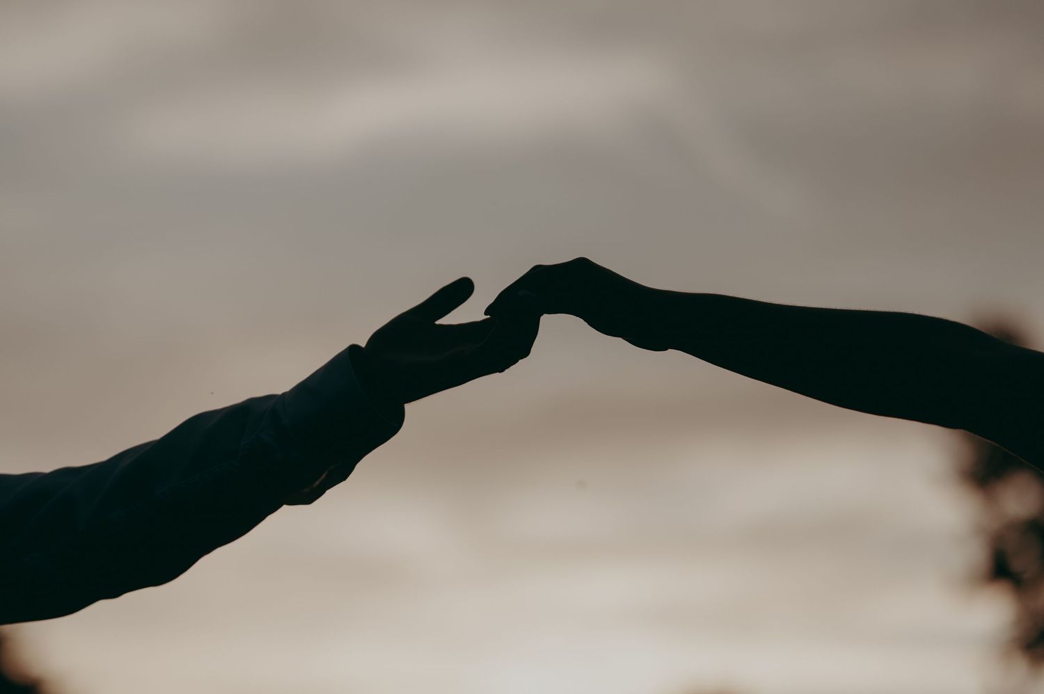 Two hands reaching toward each other in silhouette against a dramatic sunset sky, symbolizing connection and longing.