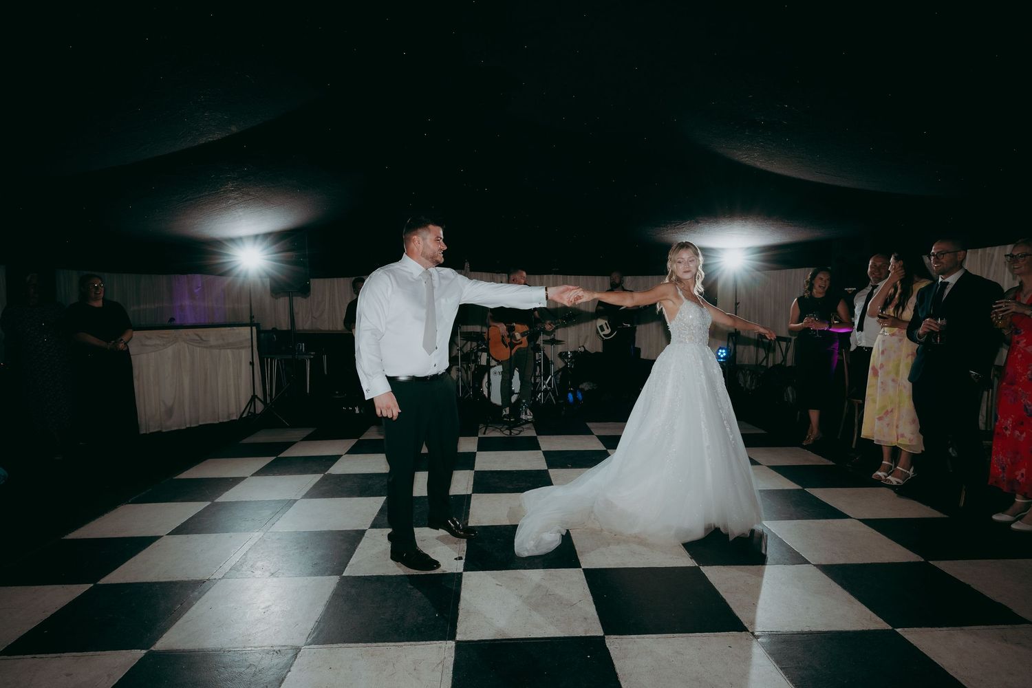 Bride and groom sharing their first dance on a black and white checkered dance floor at a wedding reception.