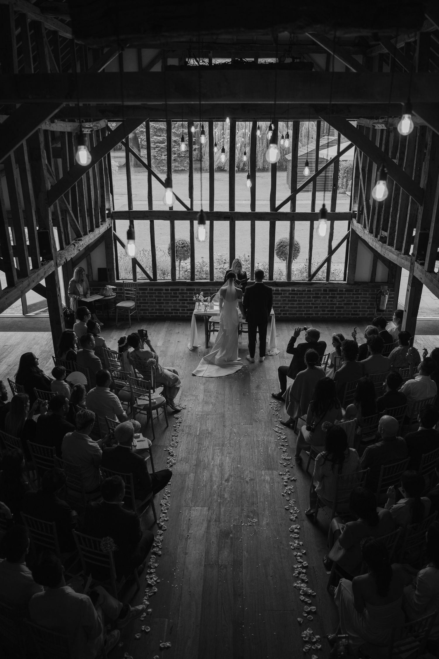 Black and white aerial view of a rustic barn wedding ceremony with guests seated as couple stands at the altar.