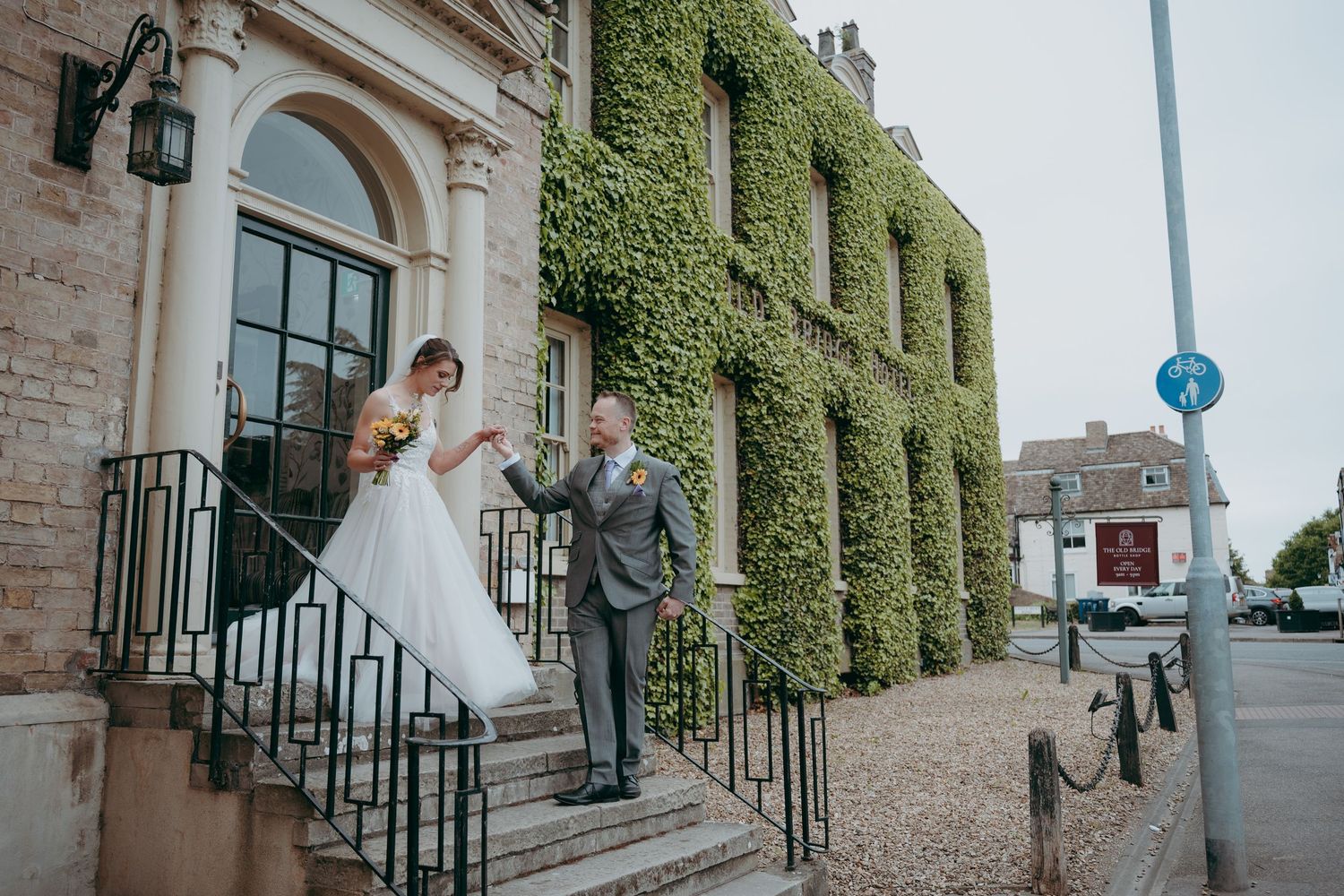 Bride and groom pose on stone steps outside an ivy-covered wedding venue on their special day.