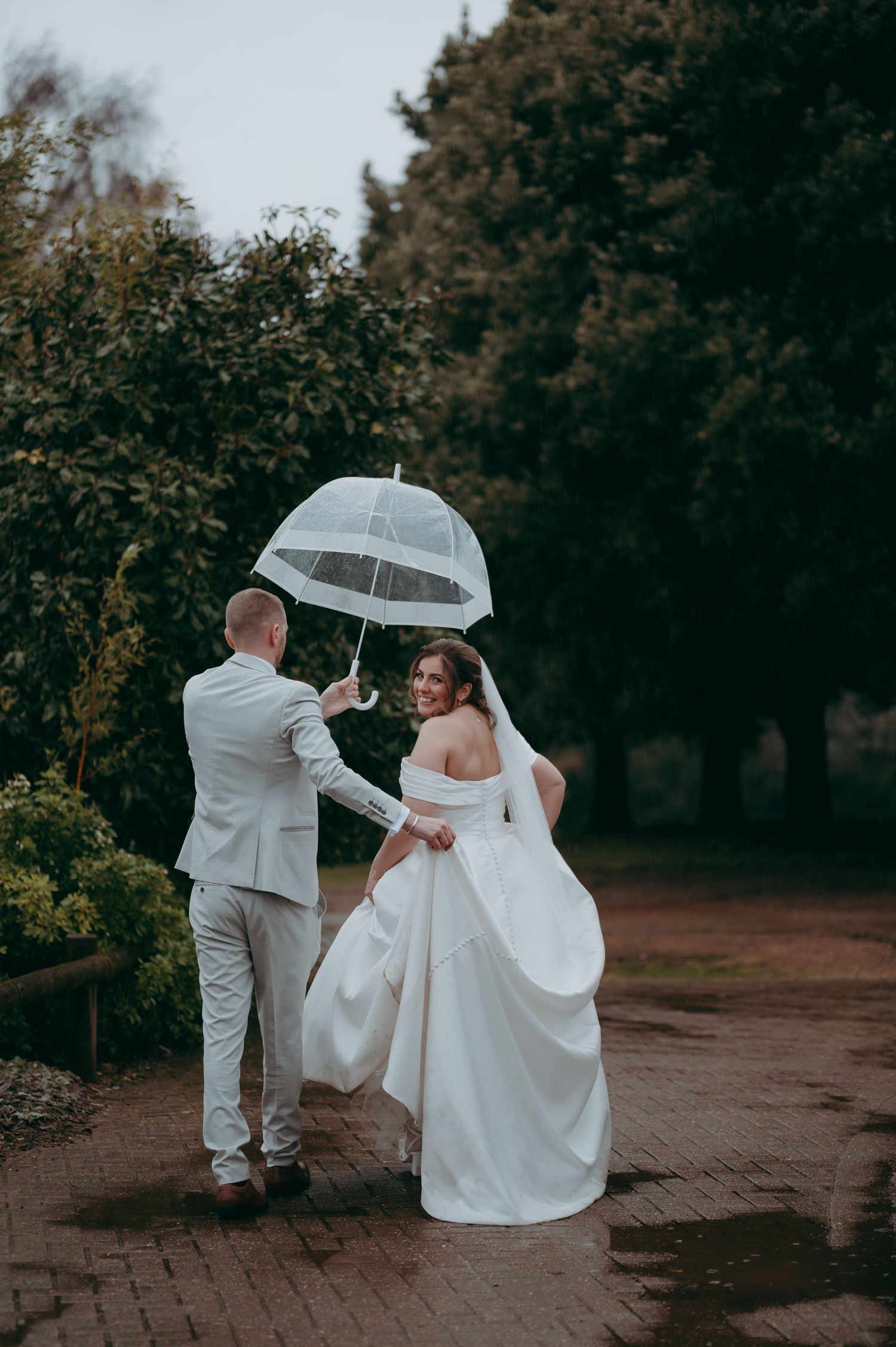 A bride and groom share a romantic embrace at sunset in a lush green field, the bride in an off-shoulder white gown.
