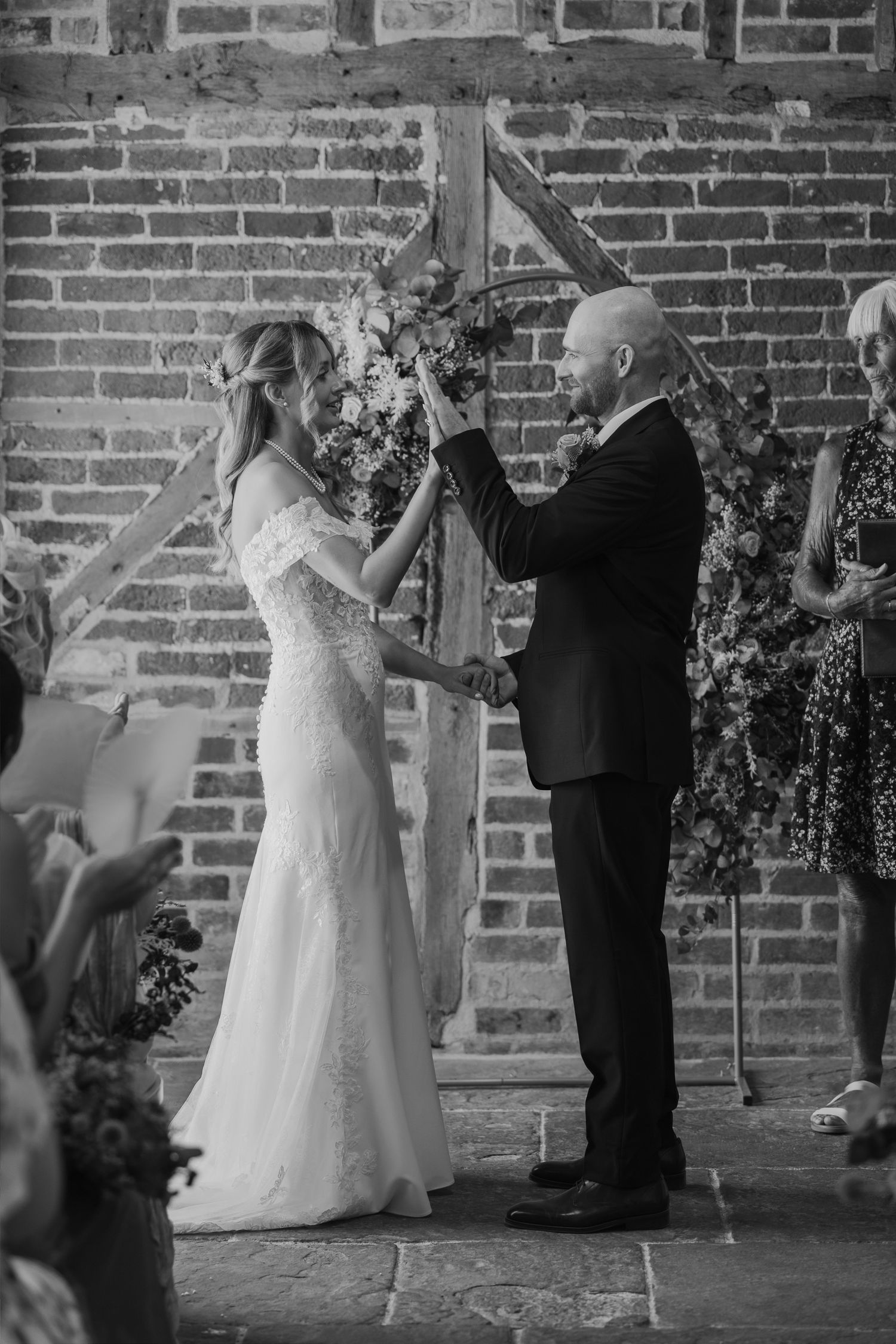Black and white photo of a bride and groom holding hands at the altar during their wedding ceremony.