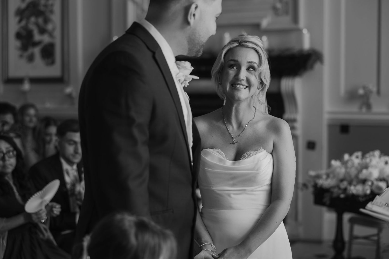 Two grooms in suits walk hand-in-hand along a tree-lined path in this elegant black and white wedding photo.