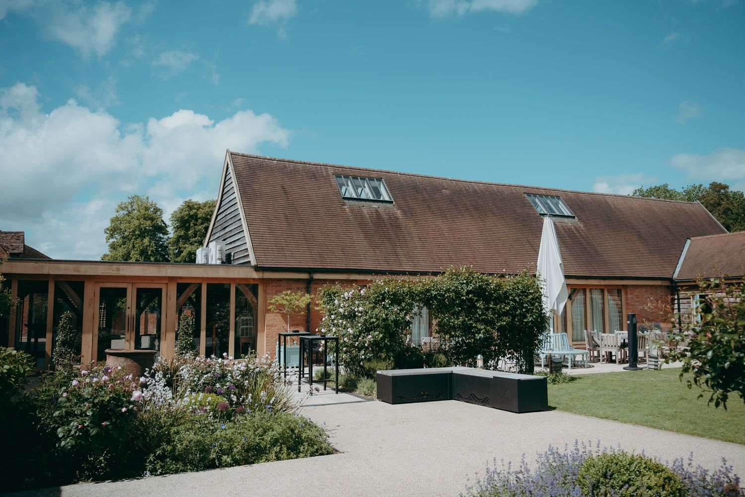 Charming barn wedding venue with rustic brick exterior, manicured gardens, and blue skies in the English countryside.