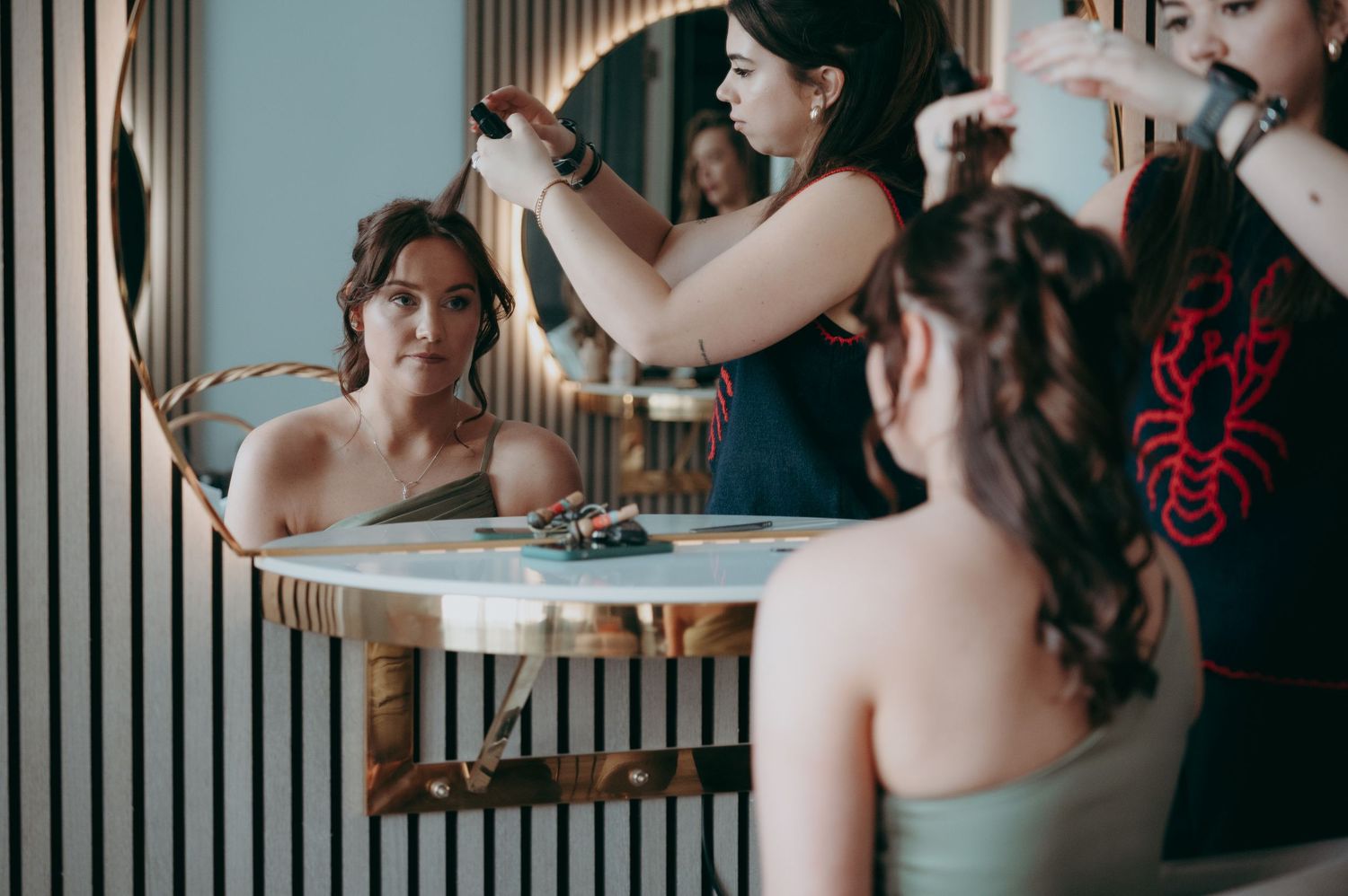 Woman getting hair styled by makeup artist in front of mirror at a salon or bridal preparation session.