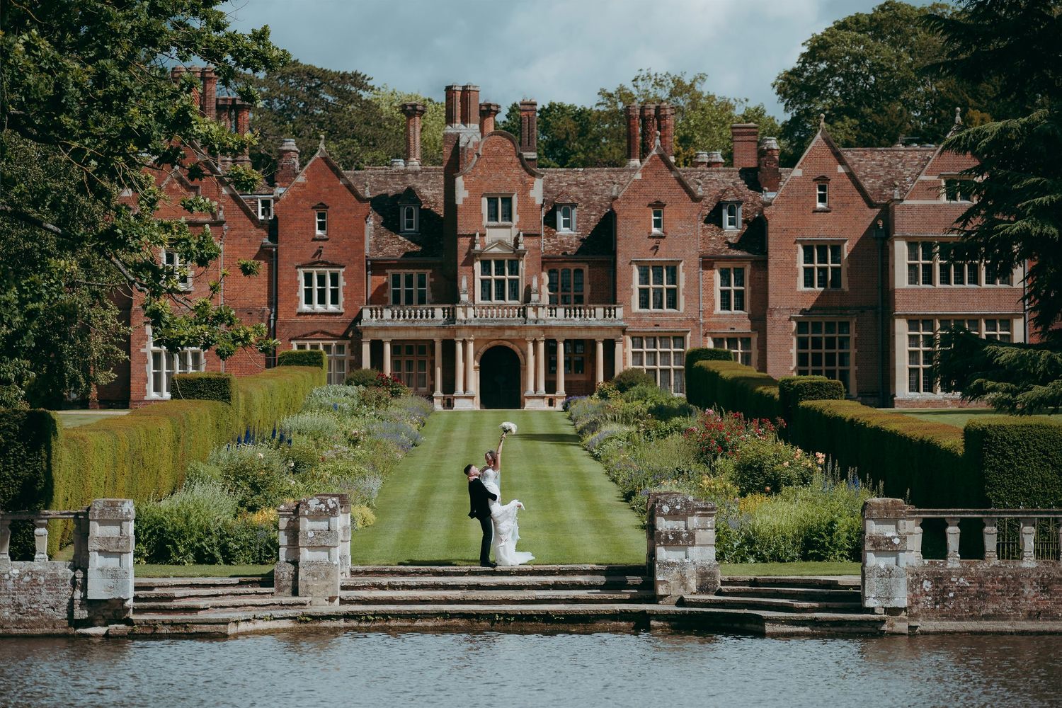 Bride and groom posing outside a stunning black and white Tudor-style wedding venue with manicured hedges.