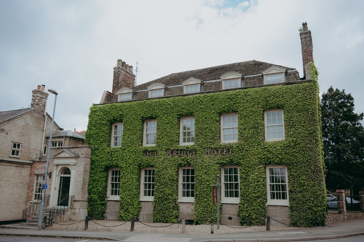 Bride and groom standing on steps of grand red brick English manor house with manicured gardens and lake.