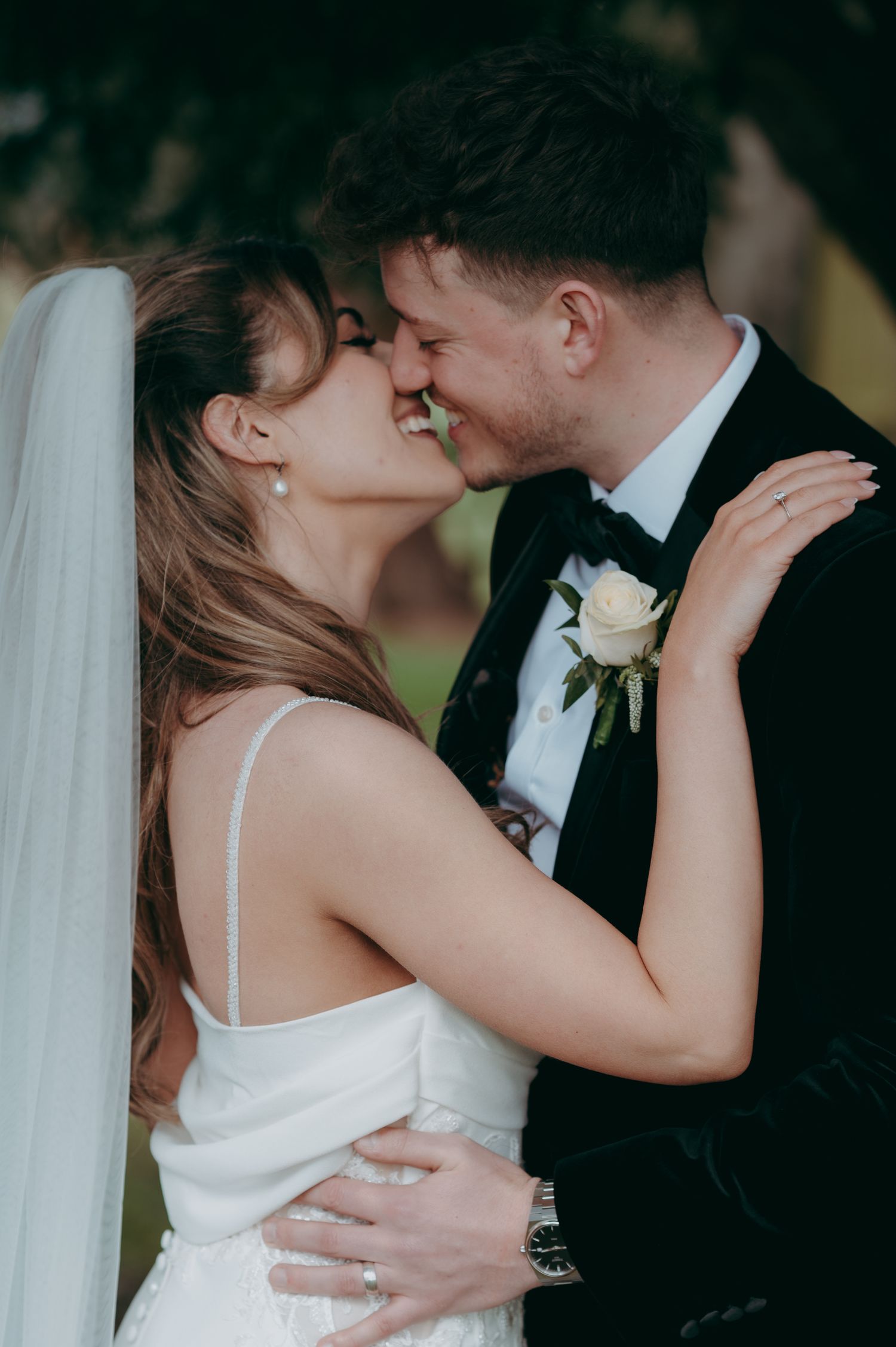 A joyful bride and groom share a romantic forehead-to-forehead moment, with her in a white gown and him in a black tuxedo.