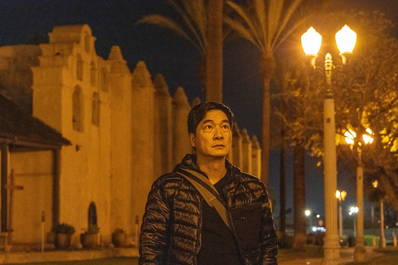 Man standing outdoors at night near illuminated street lamps and historic building.
