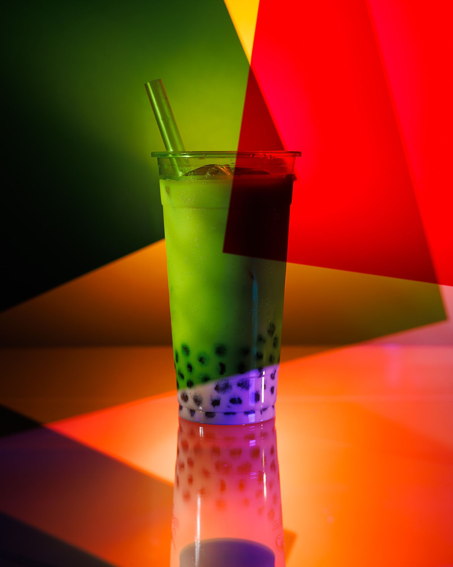 Bright green bubble tea with black pearls in vivid multicolored geometric light setting.