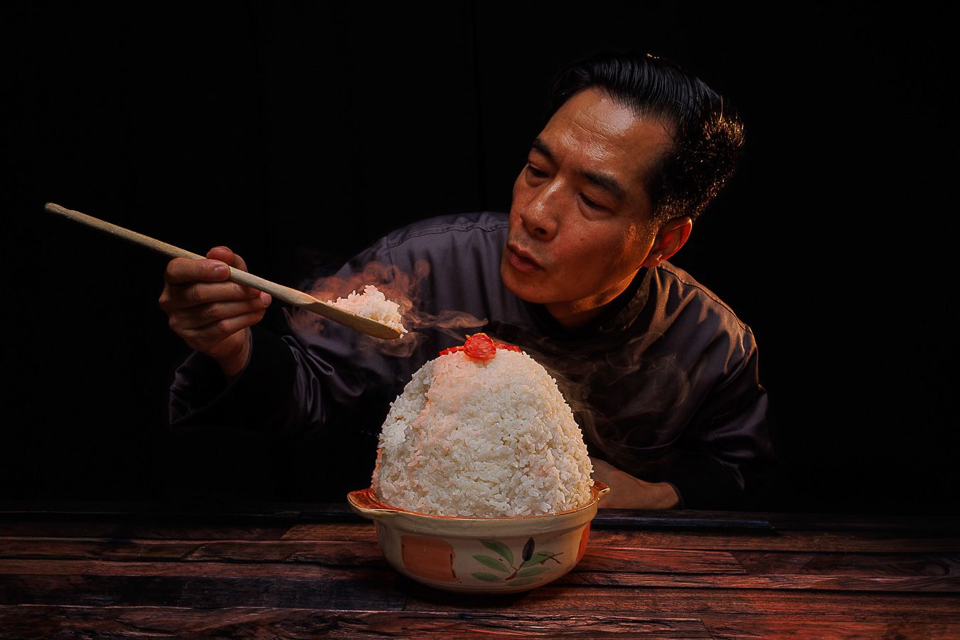 Asian man uses chopsticks to eat from a large mound of shaved ice dessert on a wooden table.