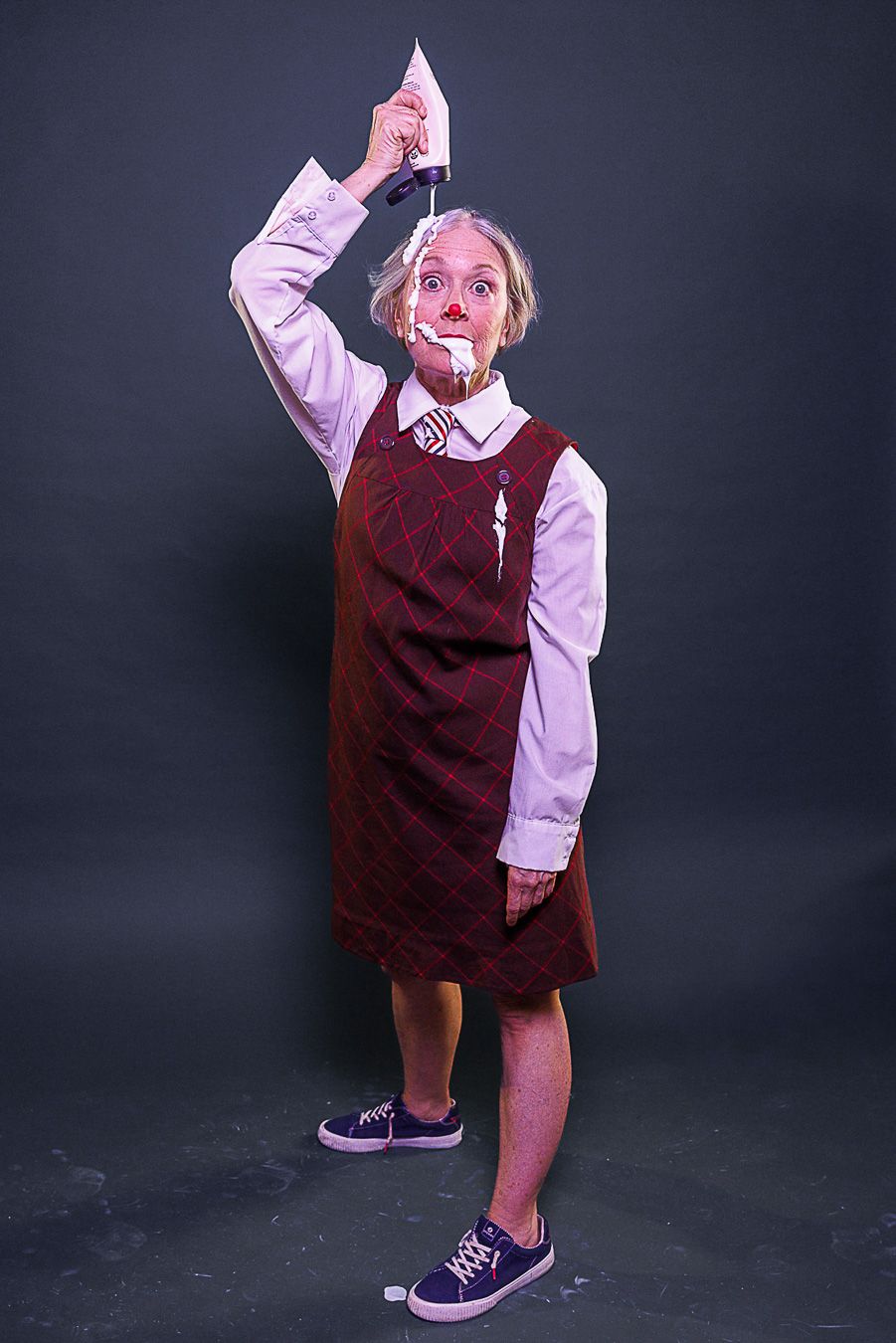 Person in clown makeup holding a knife above their head, wearing a burgundy dress over white shirt with blue sneakers.