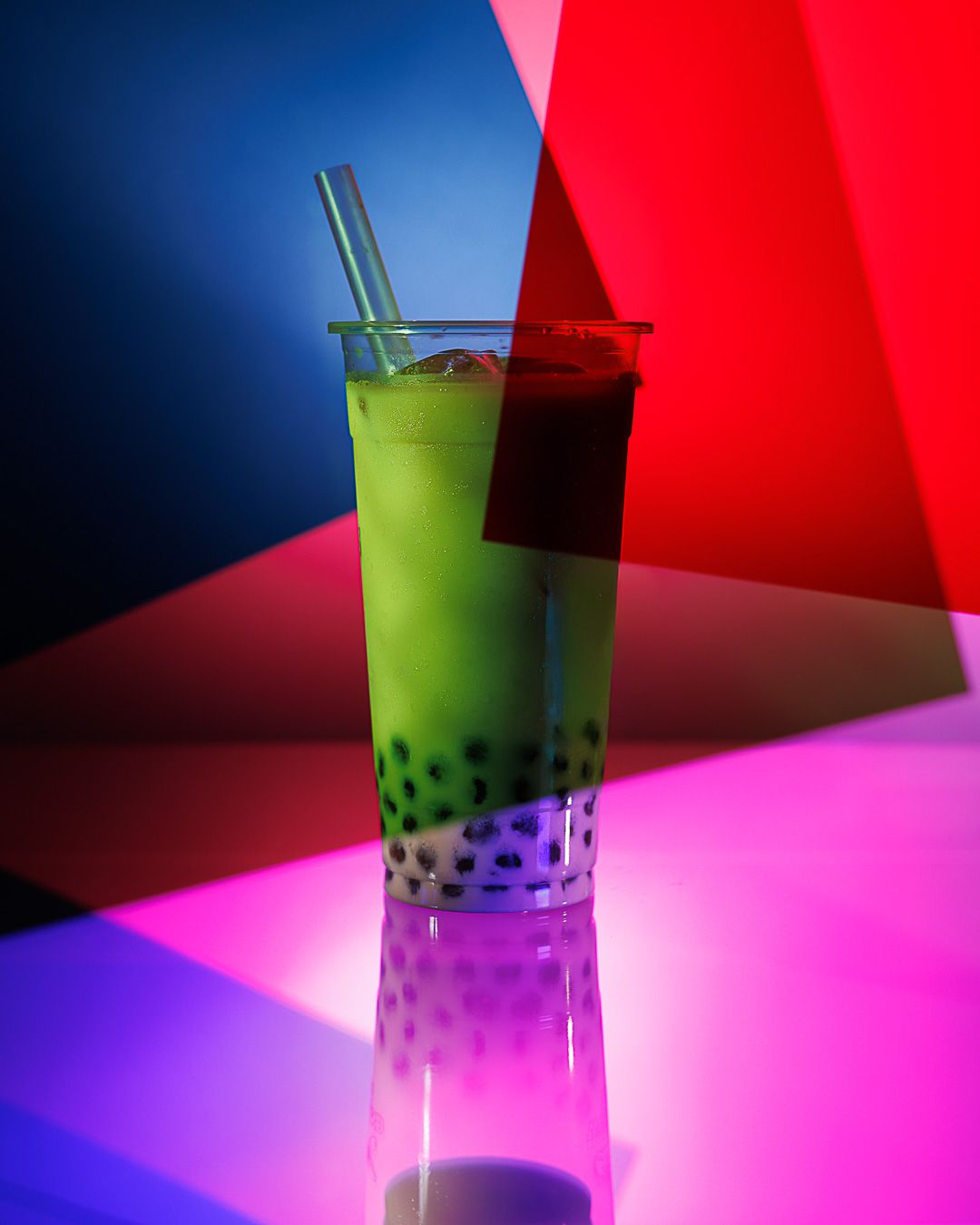 Vibrant bubble tea with green matcha and tapioca pearls in a clear cup, illuminated by colorful neon lights.