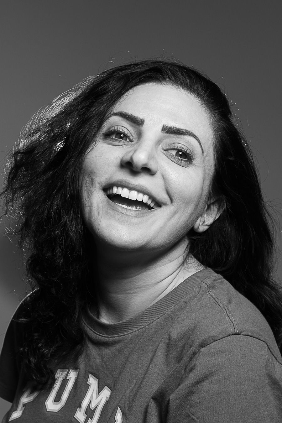 Black and white portrait of a smiling woman with dark wavy hair wearing a Puma t-shirt.