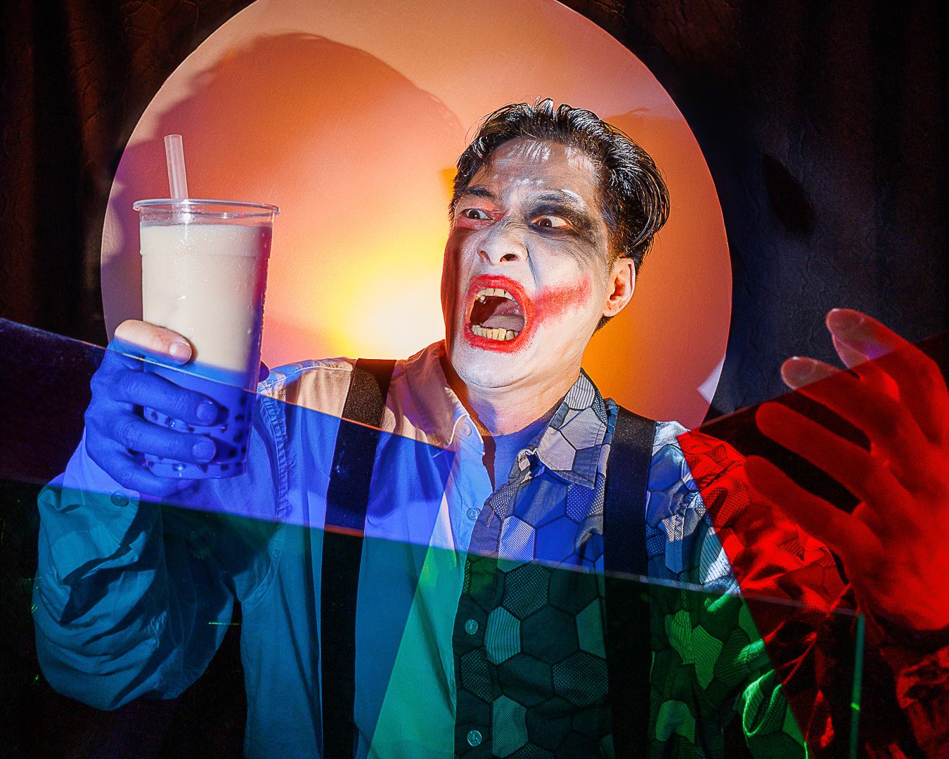Person in Joker makeup holding a milk drink, surrounded by colorful geometric shapes and dramatic lighting.