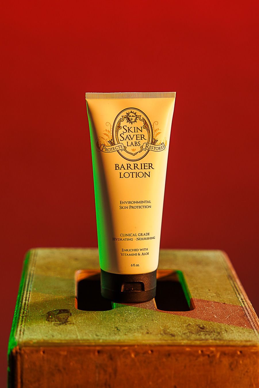 Skin Saver Labs Barrier Lotion tube for environmental skin protection, enriched with vitamins, on rustic box with red background.
