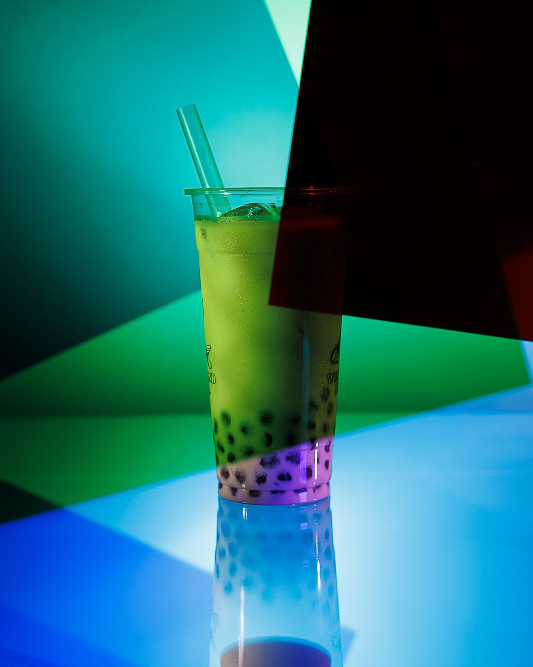 A vibrant bubble tea with green matcha and tapioca pearls in a tall cup, illuminated by colorful neon lights.