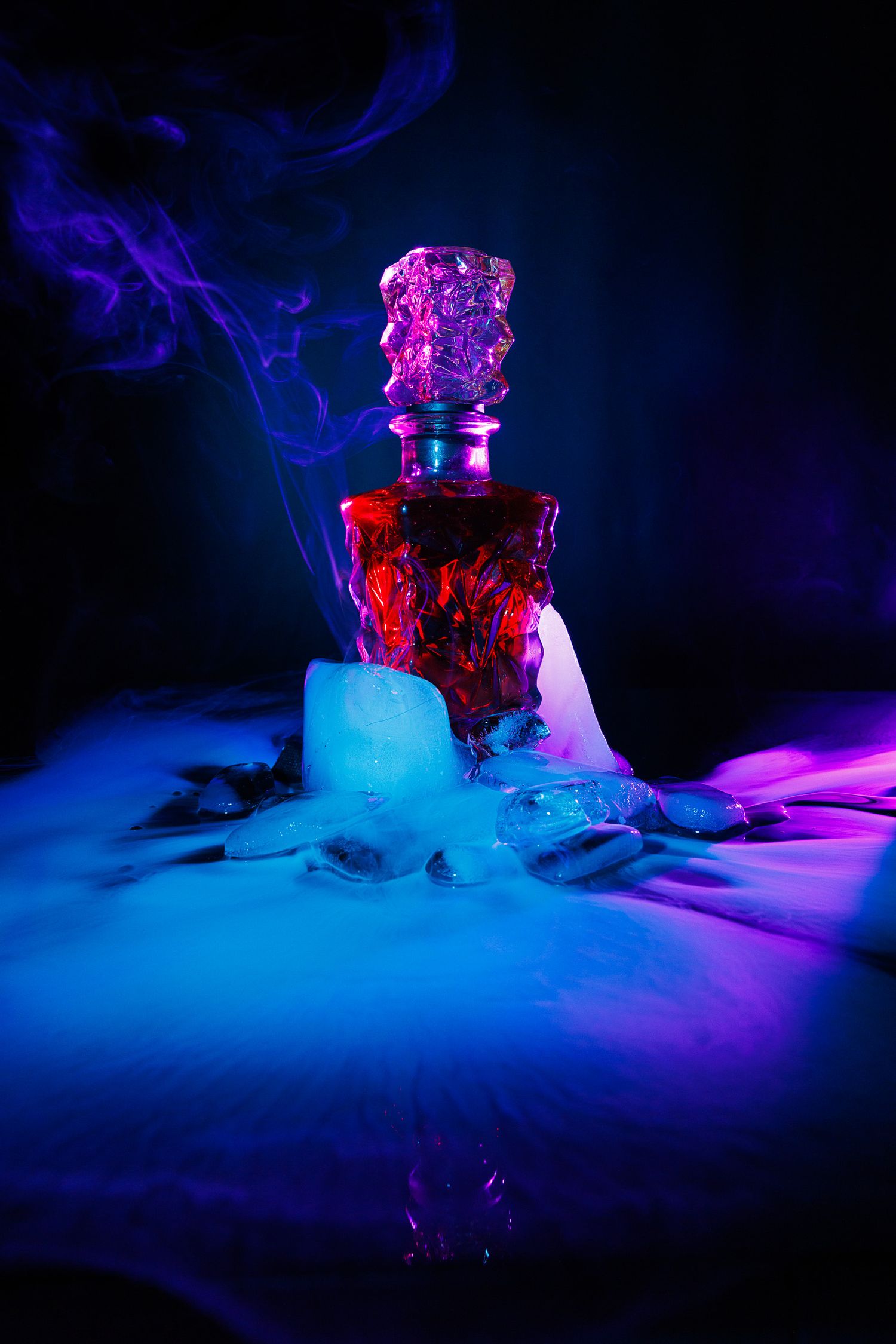 Dramatic red decorative bottle with blue smoke and ice in dark moody lighting.
