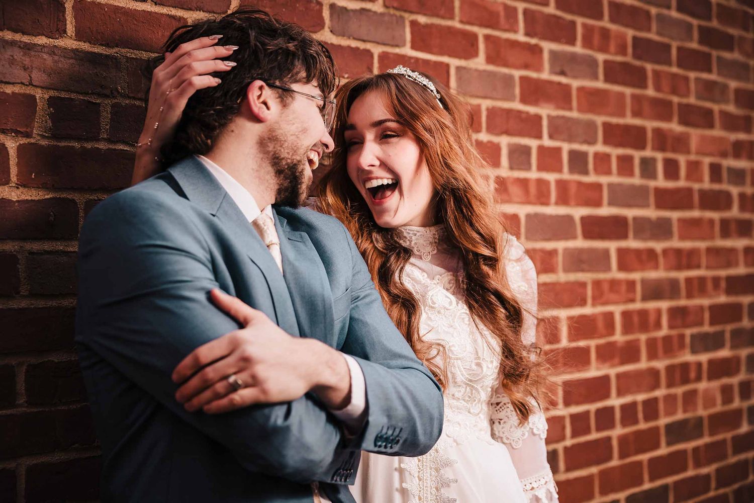 Couple laughing and embracing against a brick wall during their elopement in the North End of Boston.