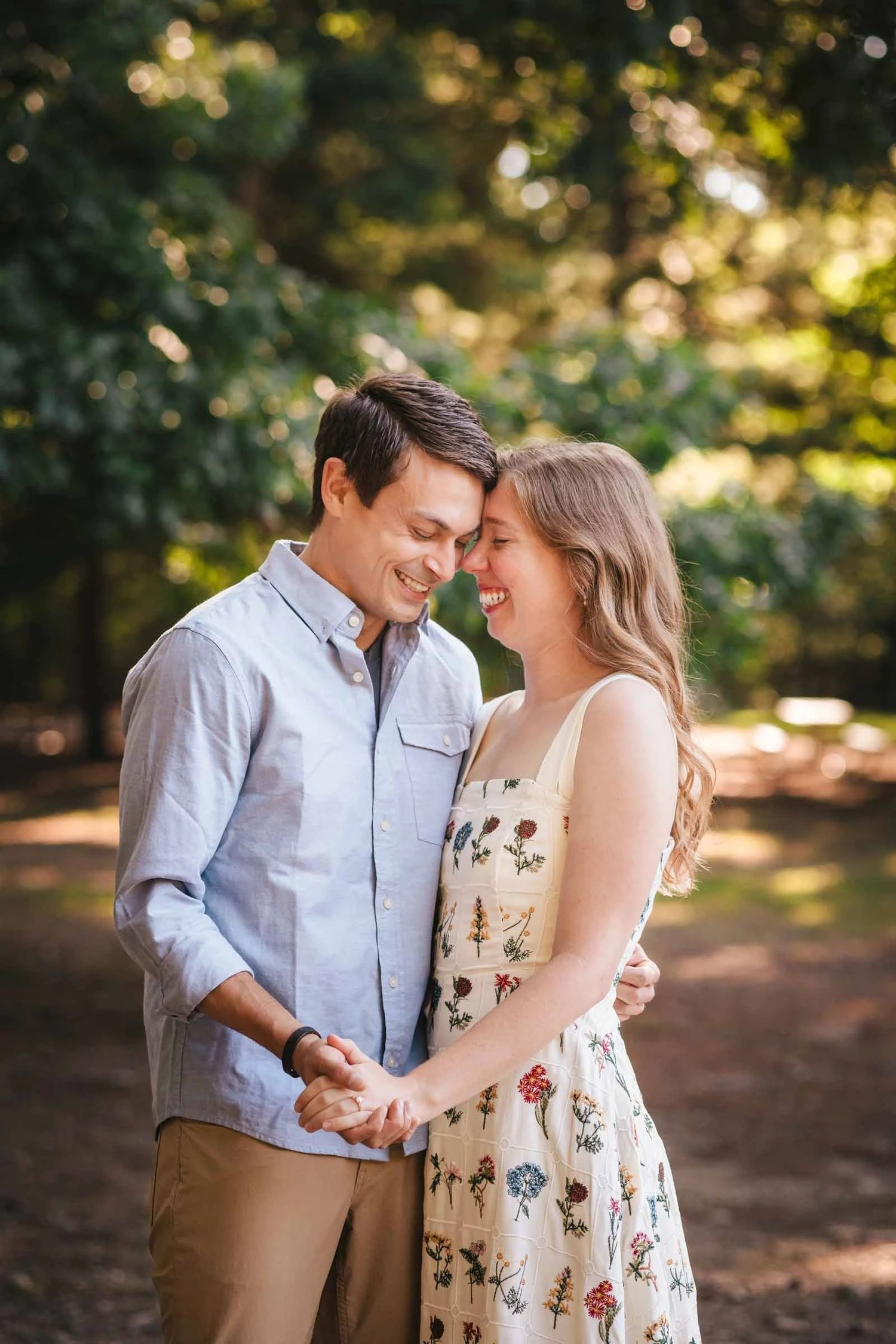 Engaged couple embracing and smiling at each other in dappled sunlight among trees. Engagement at Borderland State Park, North Easton, MA