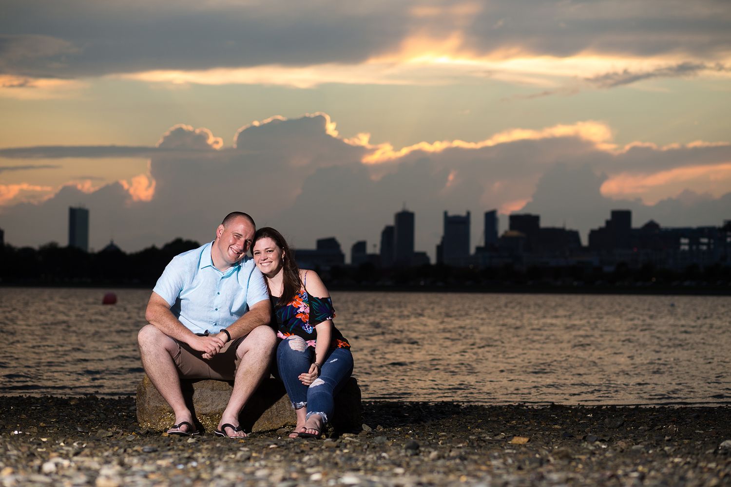 The bride and groom share a smiley portrait at sunset on Castle Island with the Boston Skyline in the background