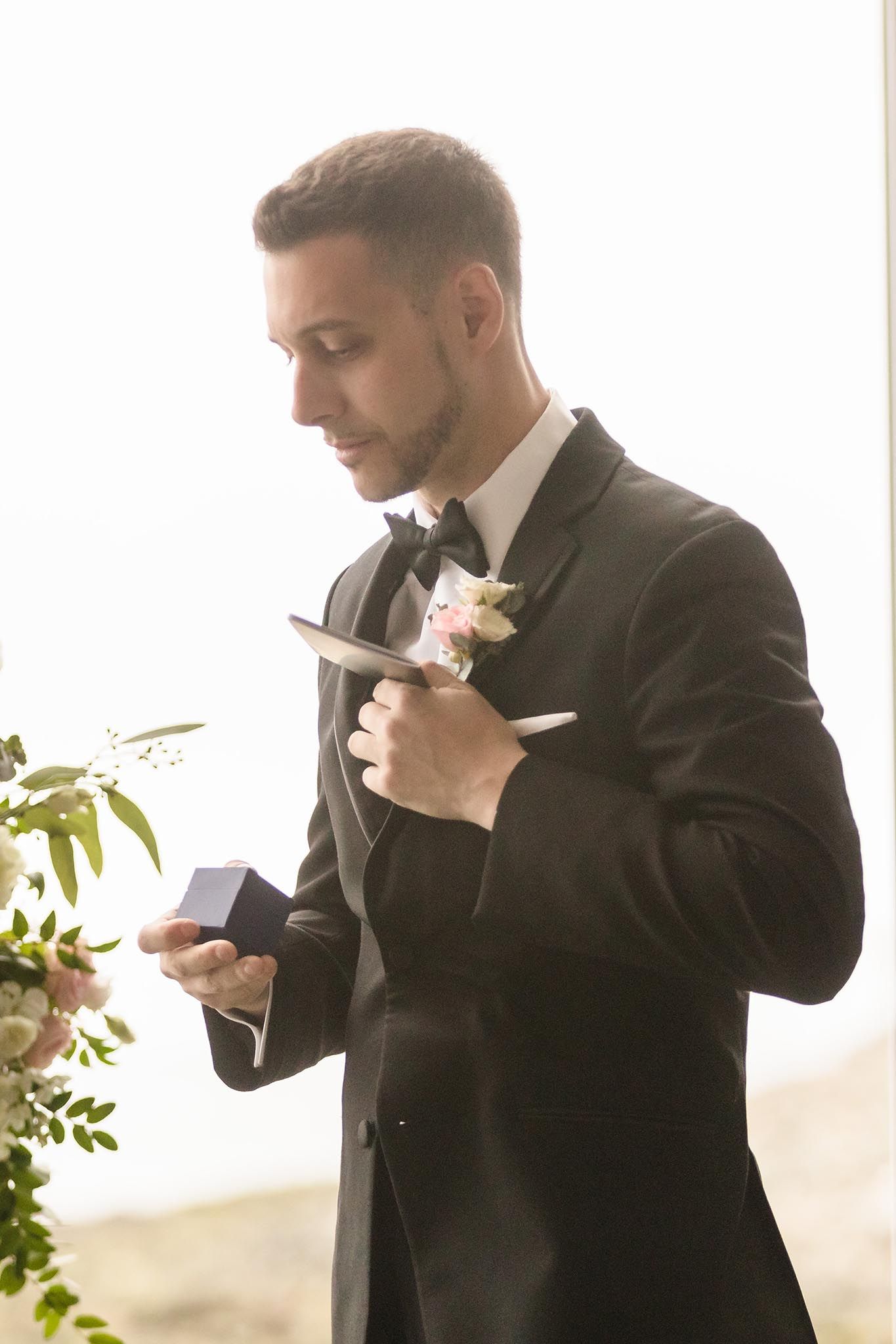 The best man pulls the wedding rings out of a box in his tux coat pocket.