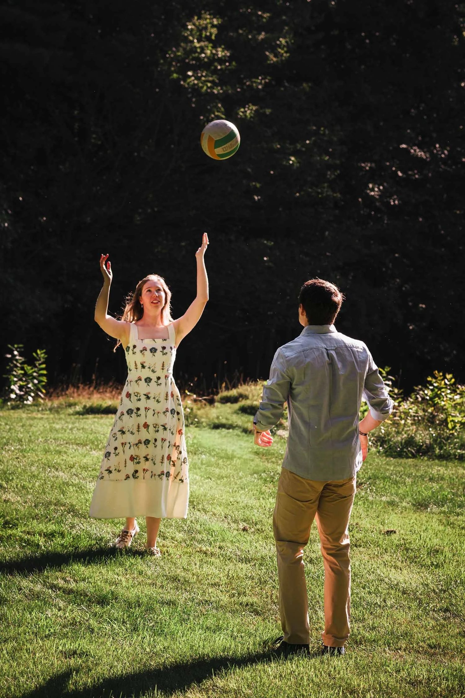 Woman and man tossing a yellow ball back and forth on a grassy lawn.  Engagement at Borderland State Park, North Easton, MA
