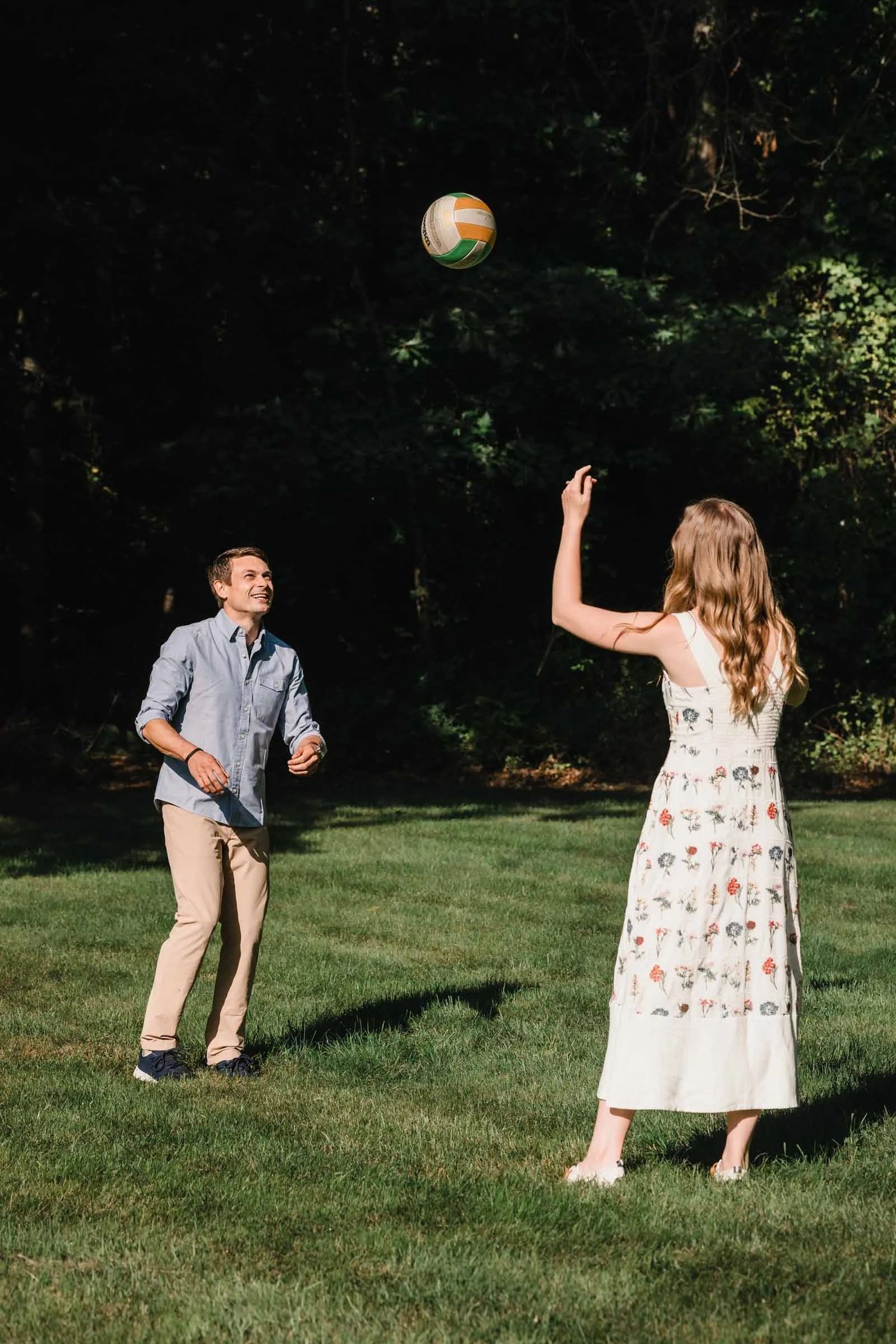 A couple playing catch with a colorful ball in a sunny backyard. Engagement at Borderland State Park, North Easton, MA
