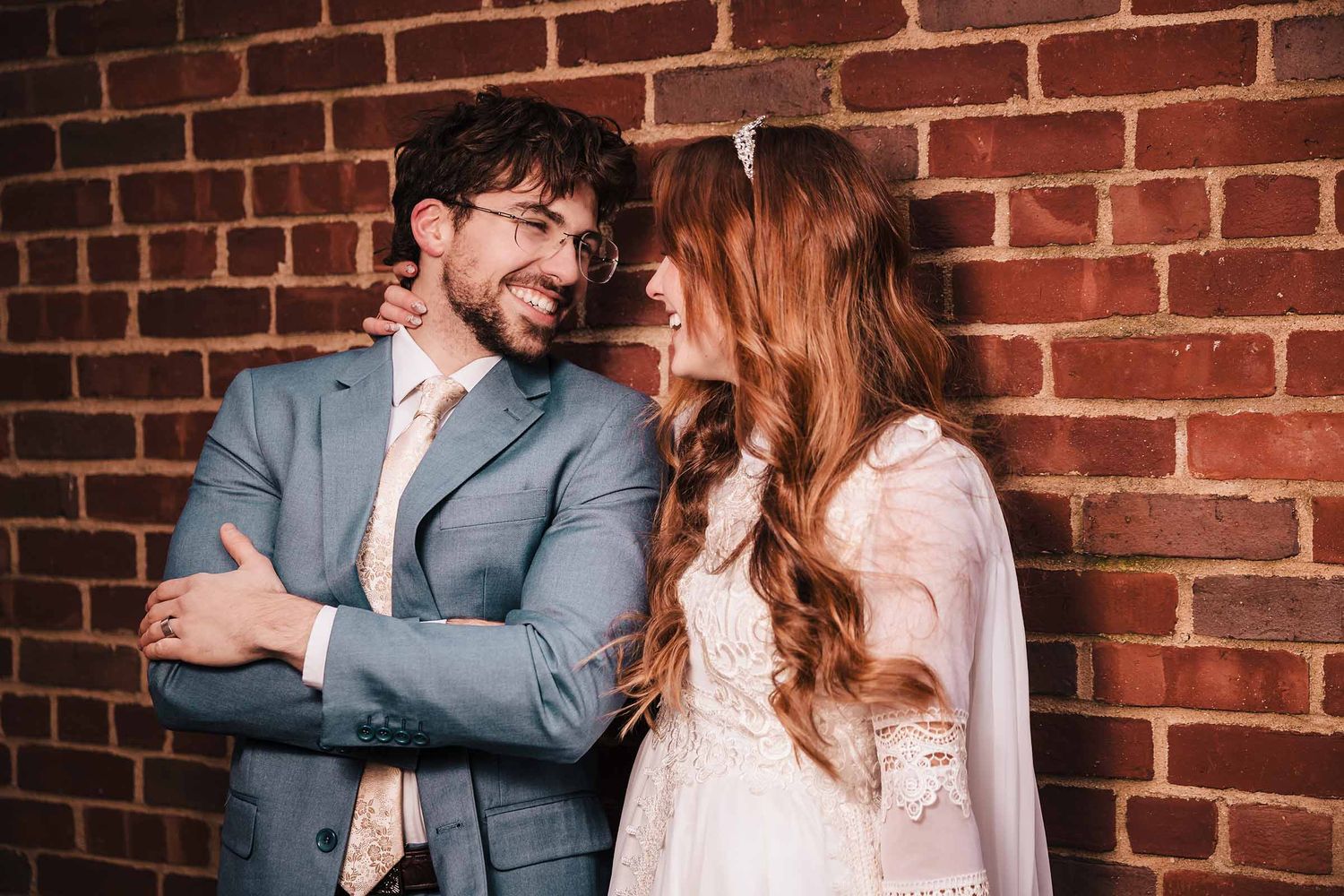 Bride and groom smile at each other during an elopement session in Boston's North end, standing close against a brick wall