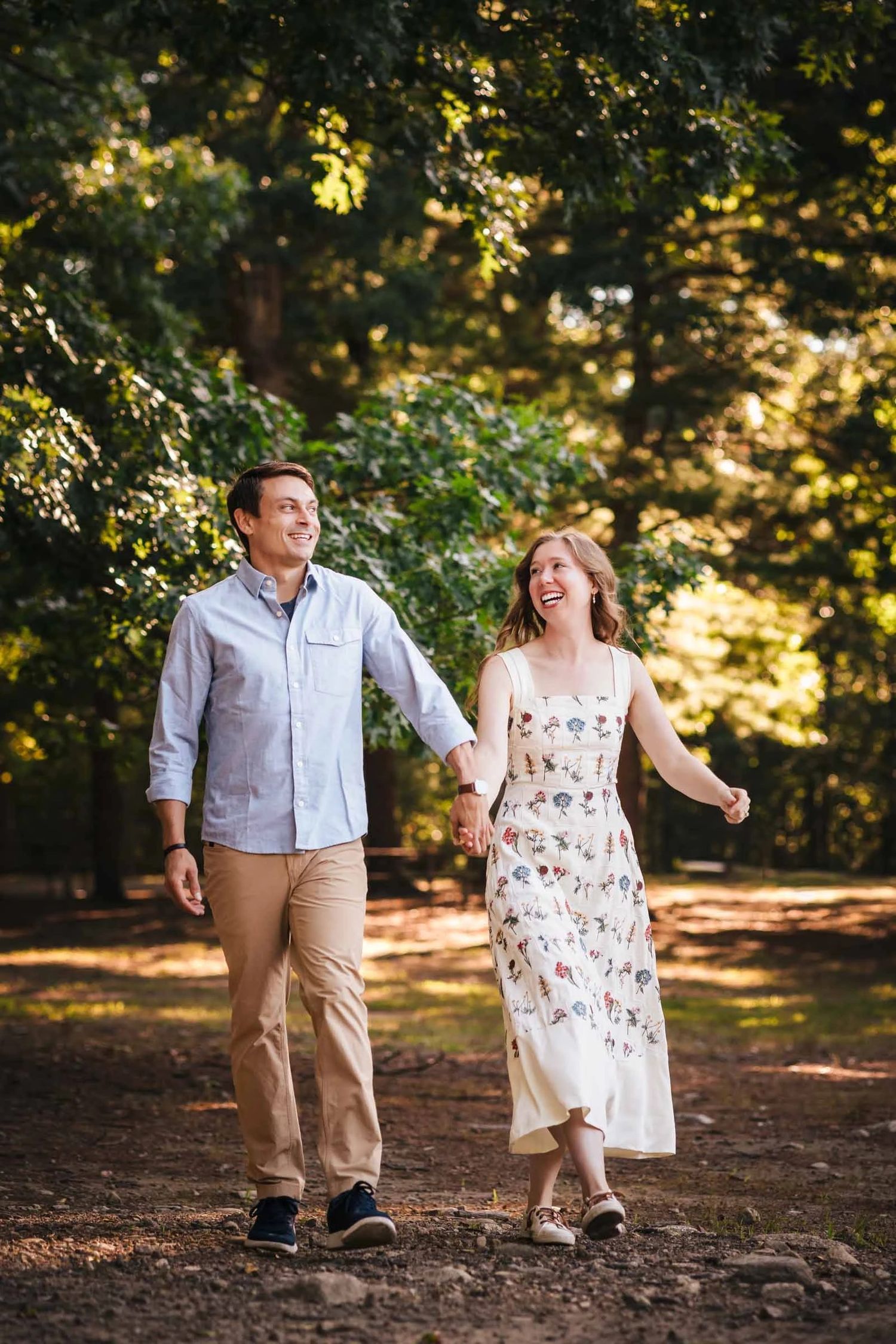 Couple walking together down a tree-lined path, holding hands and looking ahead. Engagement at Borderland State Park, North Easton, MA
