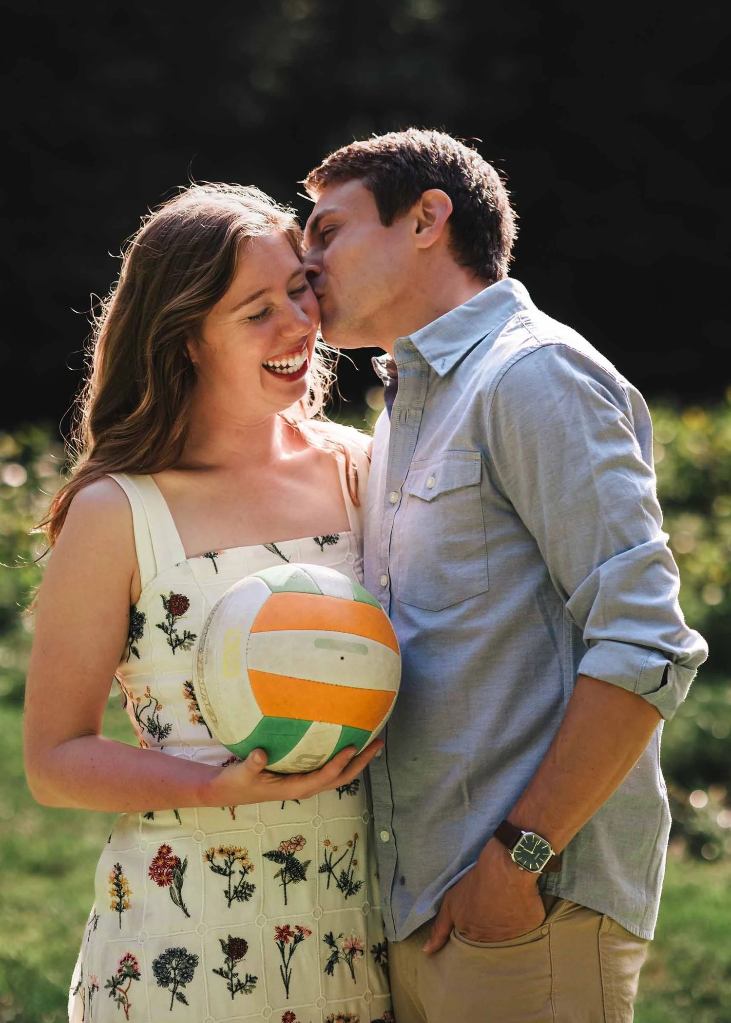 Young couple embracing outdoors, man kissing woman's cheek while she holds a volleyball and smiles. Engagement at Borderland State Park