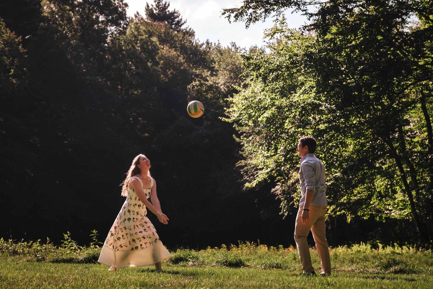 A couple playing volleyball in a sunlit meadow, the ball suspended mid-air between them. Engagement at Borderland State Park, North Easton