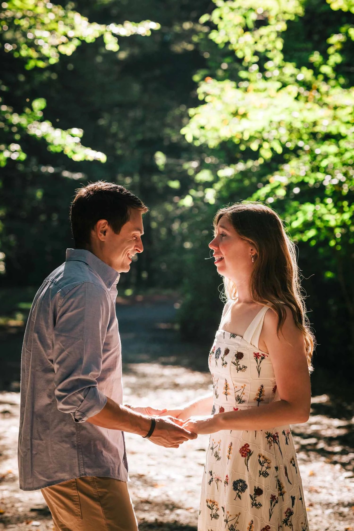 A couple holds hands and gazes at each other in dappled woodland light. Engagement at Borderland State Park, North Easton, MA