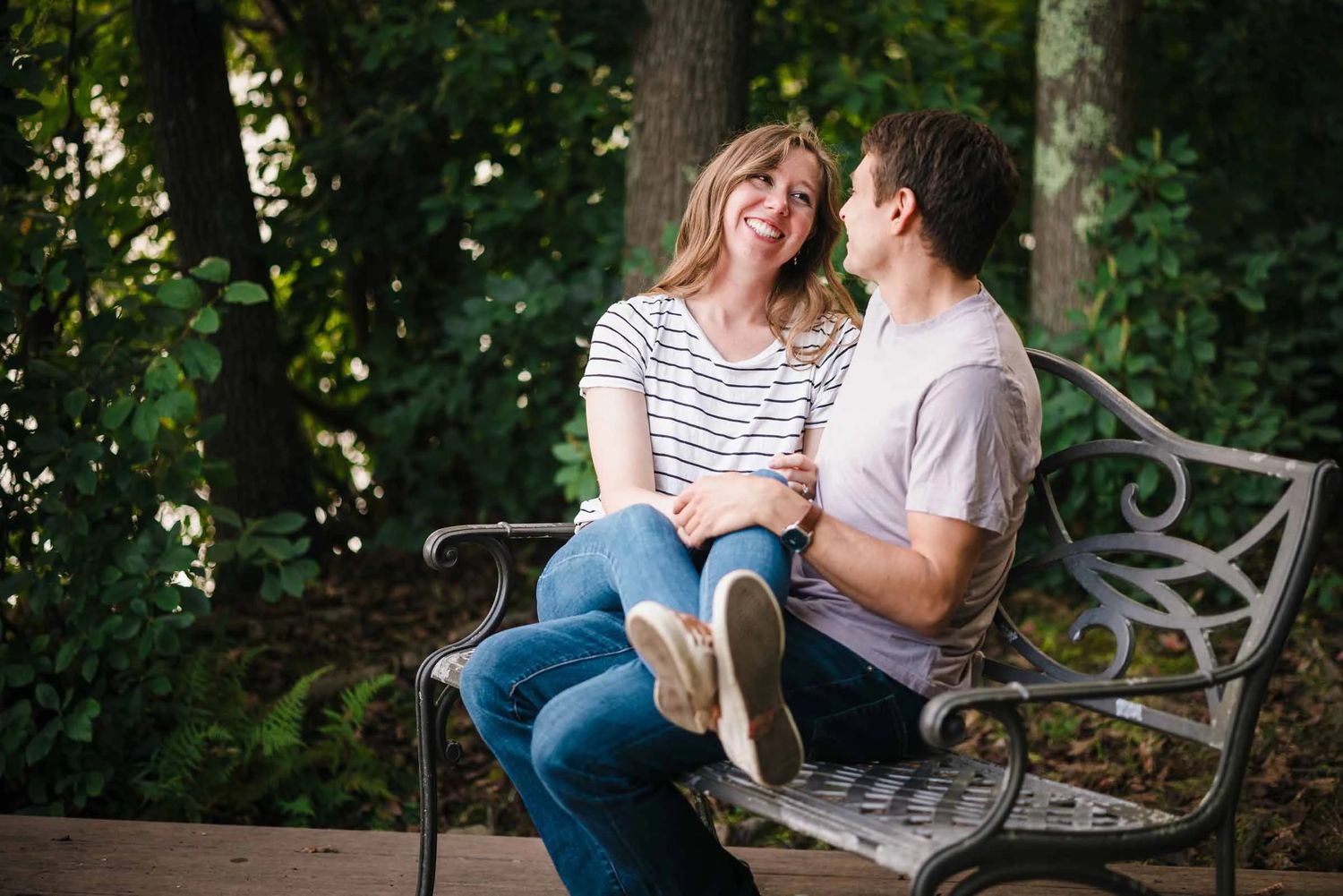 A couple sits together on a bench, smiling and gazing at each other in an intimate moment. Engagement at Borderland State Park