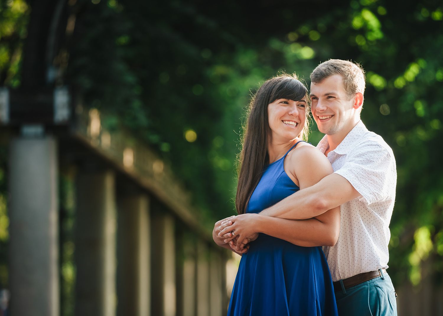 A couple poses in from the of green covered trellis at Christopher Columbus Park
