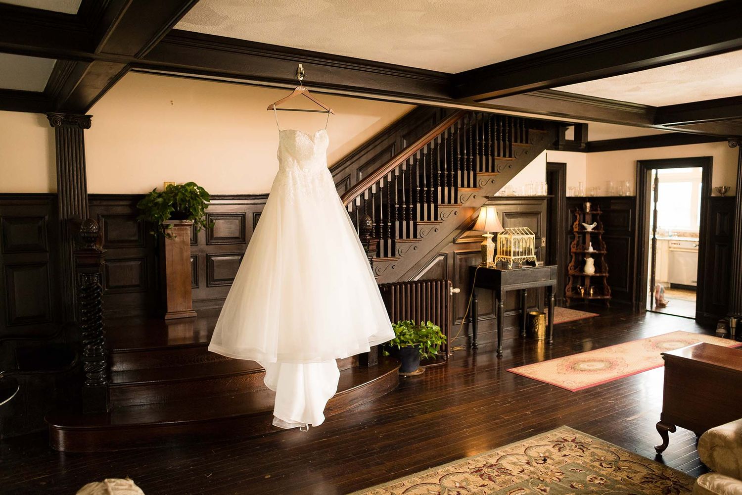 The wedding dress hangs in front of the grand staircase in the Parlor of Peirce Farm.