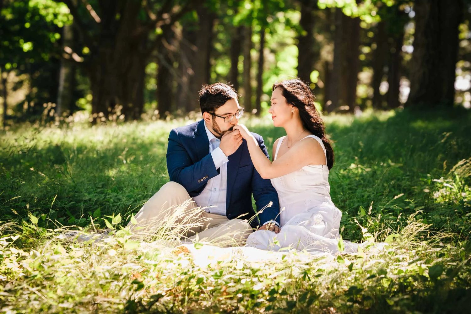 Couple sitting together for their engagement session, the groom kissing bride's hand romantically.