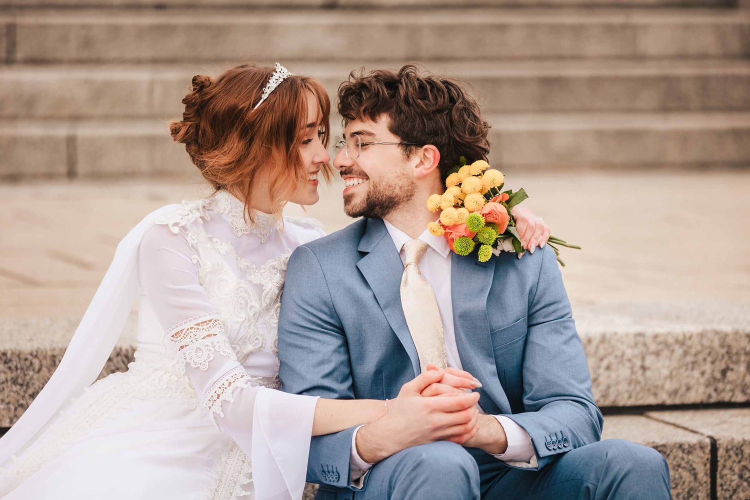 Bride and groom sitting on stone steps, sharing a romantic moment with a colorful bouquet.
