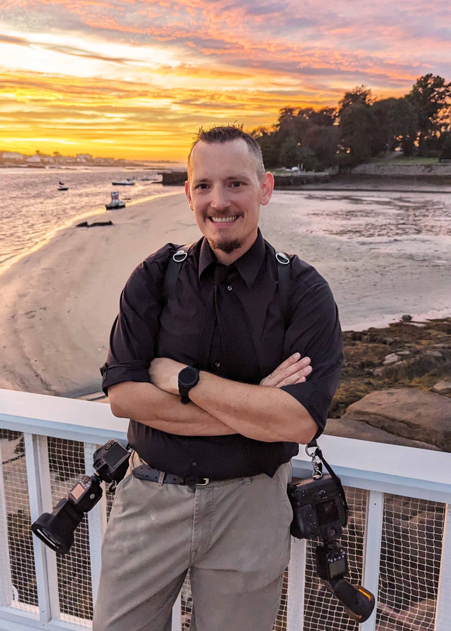 Candid headshot of Boston Wedding Photographer Gregory Hitchcock standing with arms crossed infront of a colorful sunset.