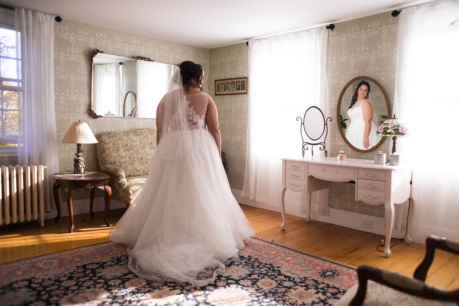 The bride, in her wedding dress, looks at herself in the mirror of her bridal suite at Peirce Farm.