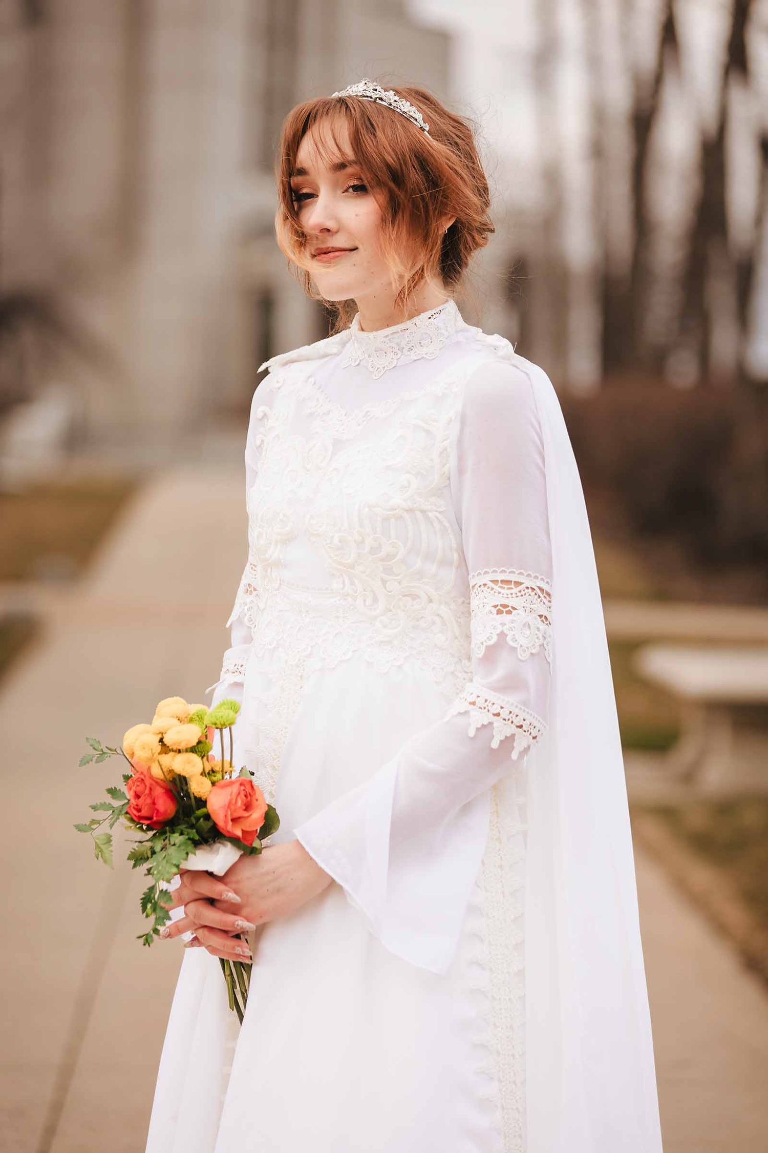 Bride in elopement ceremony attire holds a vibrant bouquet while standing alone on a Belmont street, gazing thoughtfully to the side