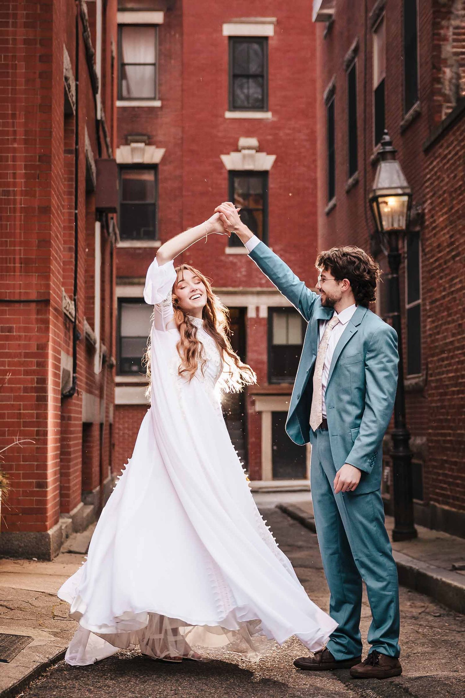 Bride and groom dancing in a brick alley Boston's North End, her dress swirling as he spins her during their elopement
