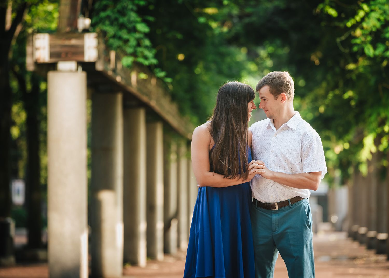 The bride and groom hold hands as they walk through the trellis in Christopher Columbus Park