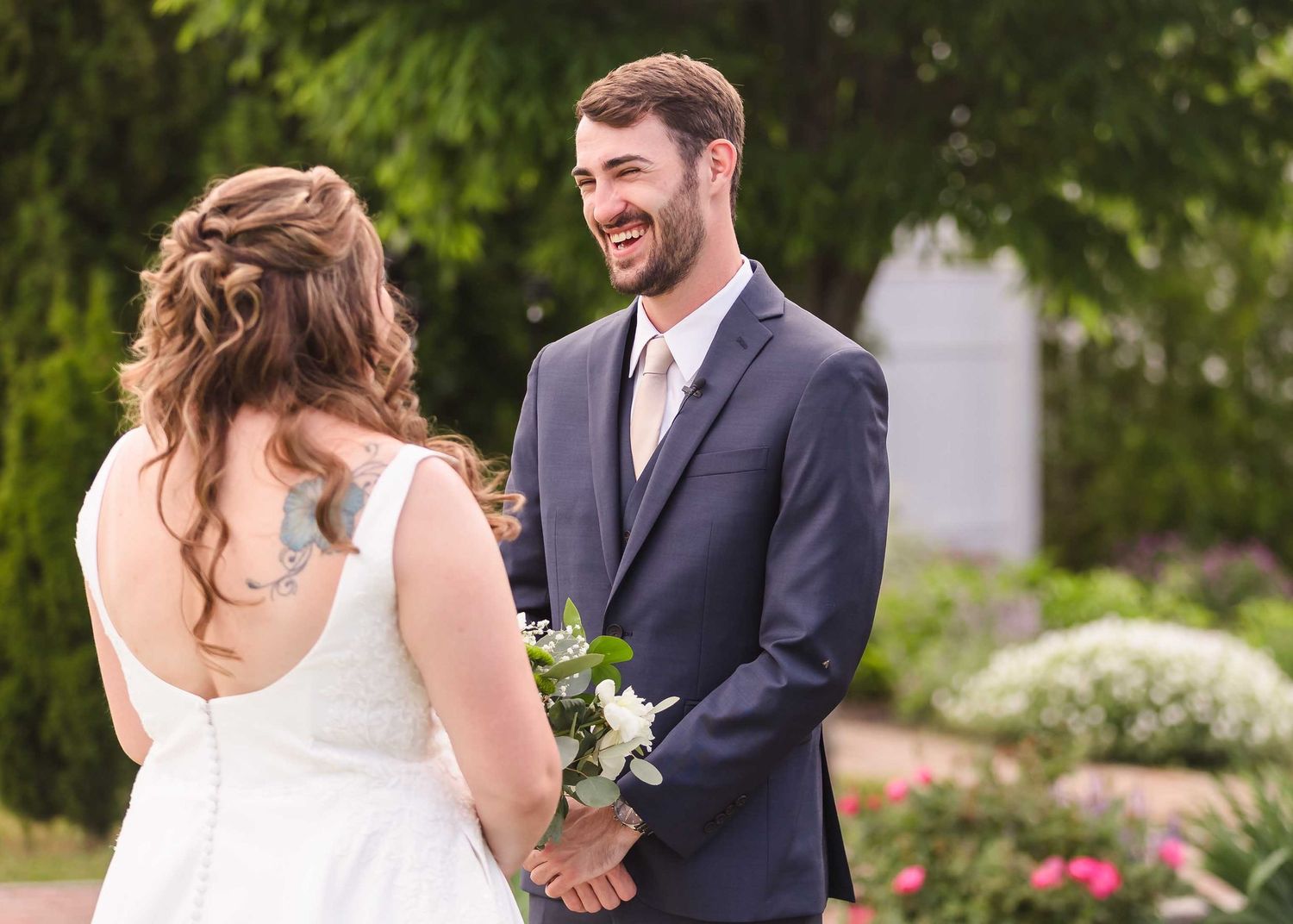 A groom is showing a joyous smile as he sees his wife for the first time on their wedding day.