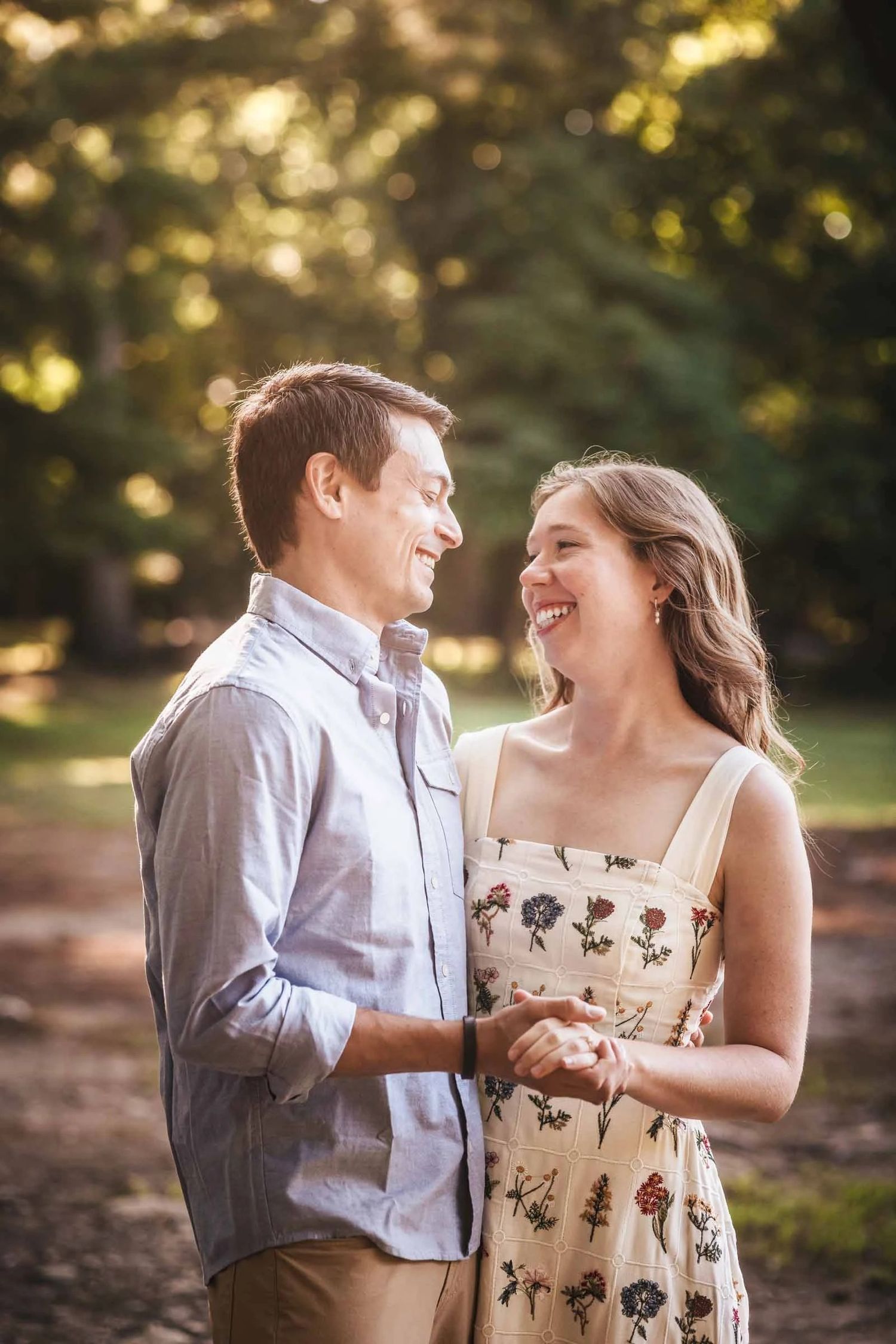 Young couple holding hands and gazing at each other outdoors in golden afternoon light. Engagement at Borderland State Park, North Easton MA