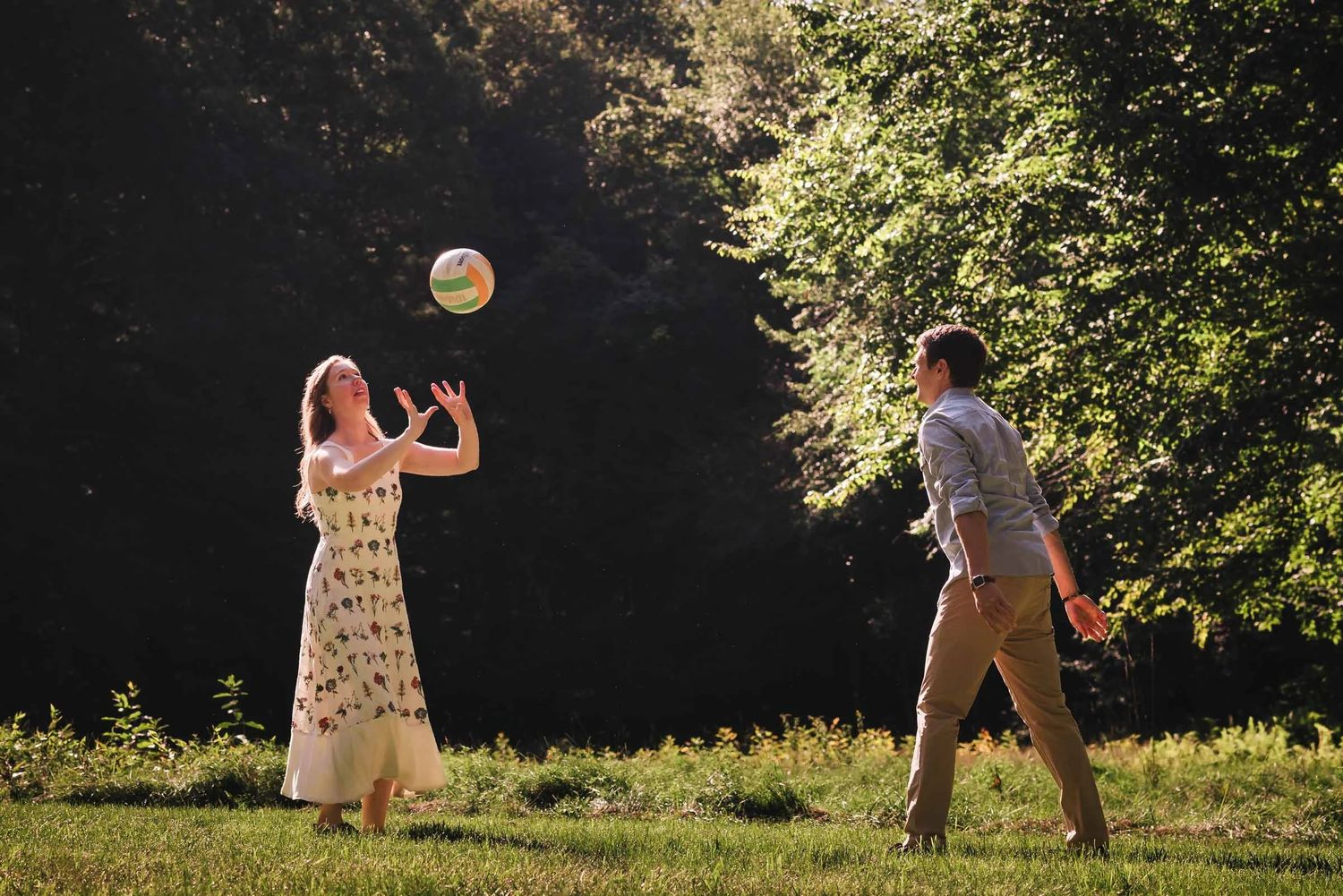 Woman and man tossing a beach ball back and forth in a sunlit grassy field.  Engagement at Borderland State Park, North Easton, MA